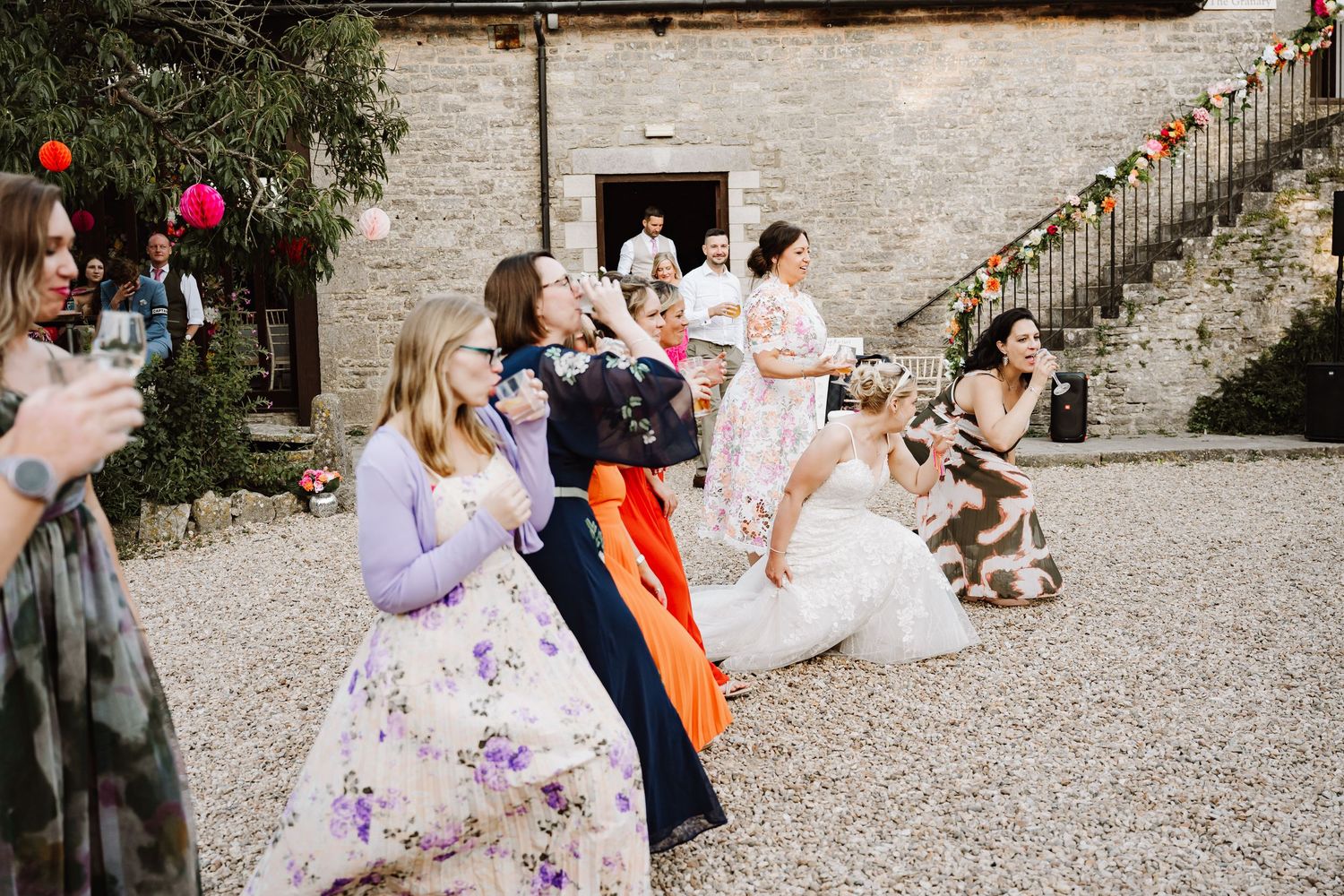 Wedding guests laugh and dance in rustic stone courtyard decorated with colorful garlands.