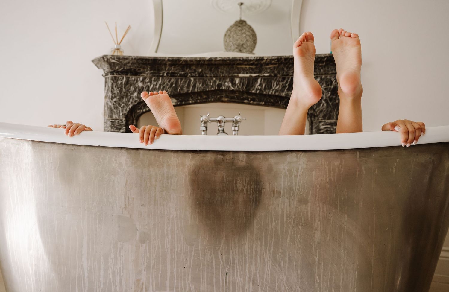 Children playfully posing in a freestanding silver bathtub with feet up near a fireplace at Pennsylvania Castle, Portland Dorset