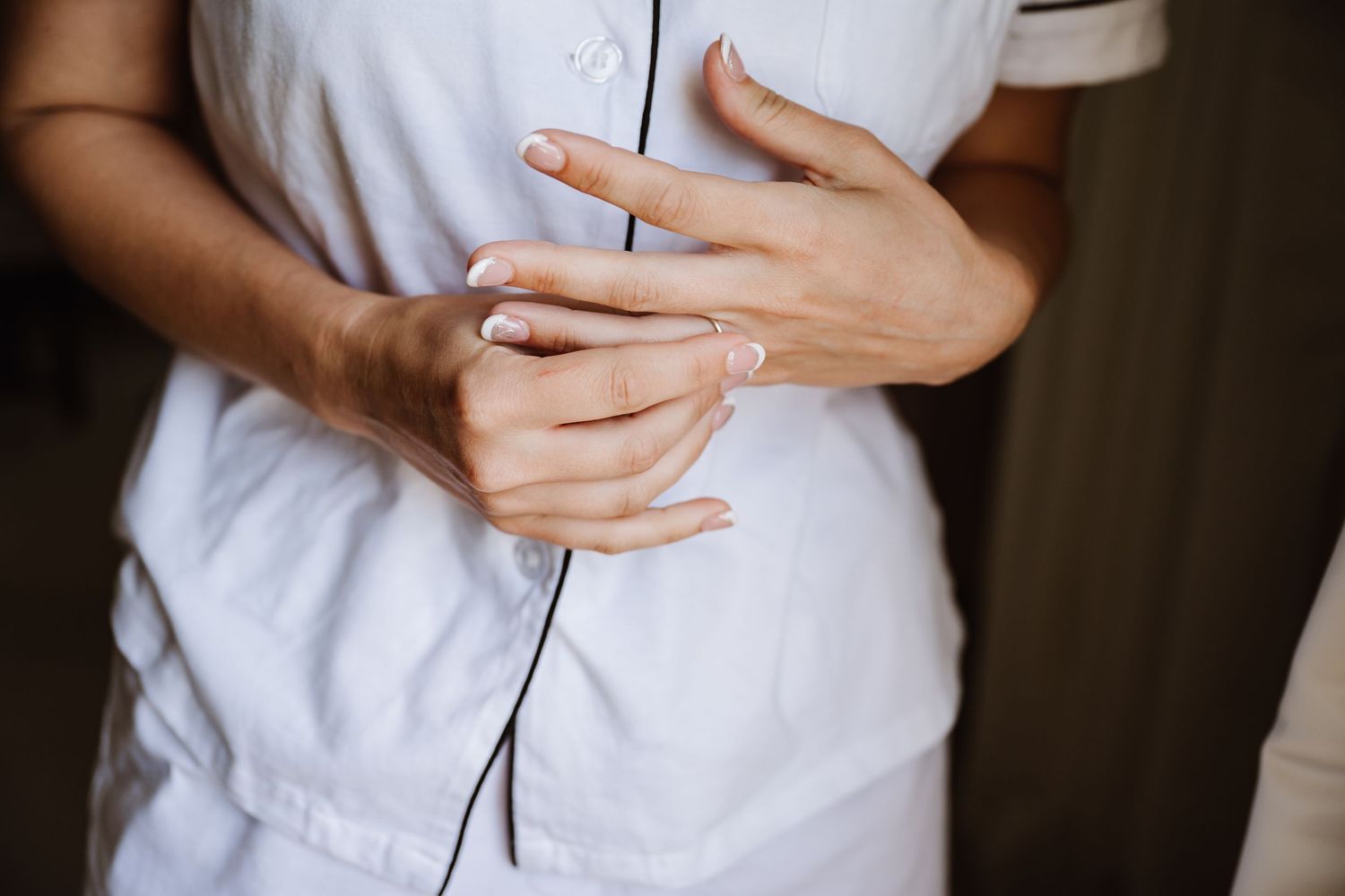 Close-up of bride's hands with French manicure clasped together over white pajamas at Pennsylvania Castle, Portland Dorset