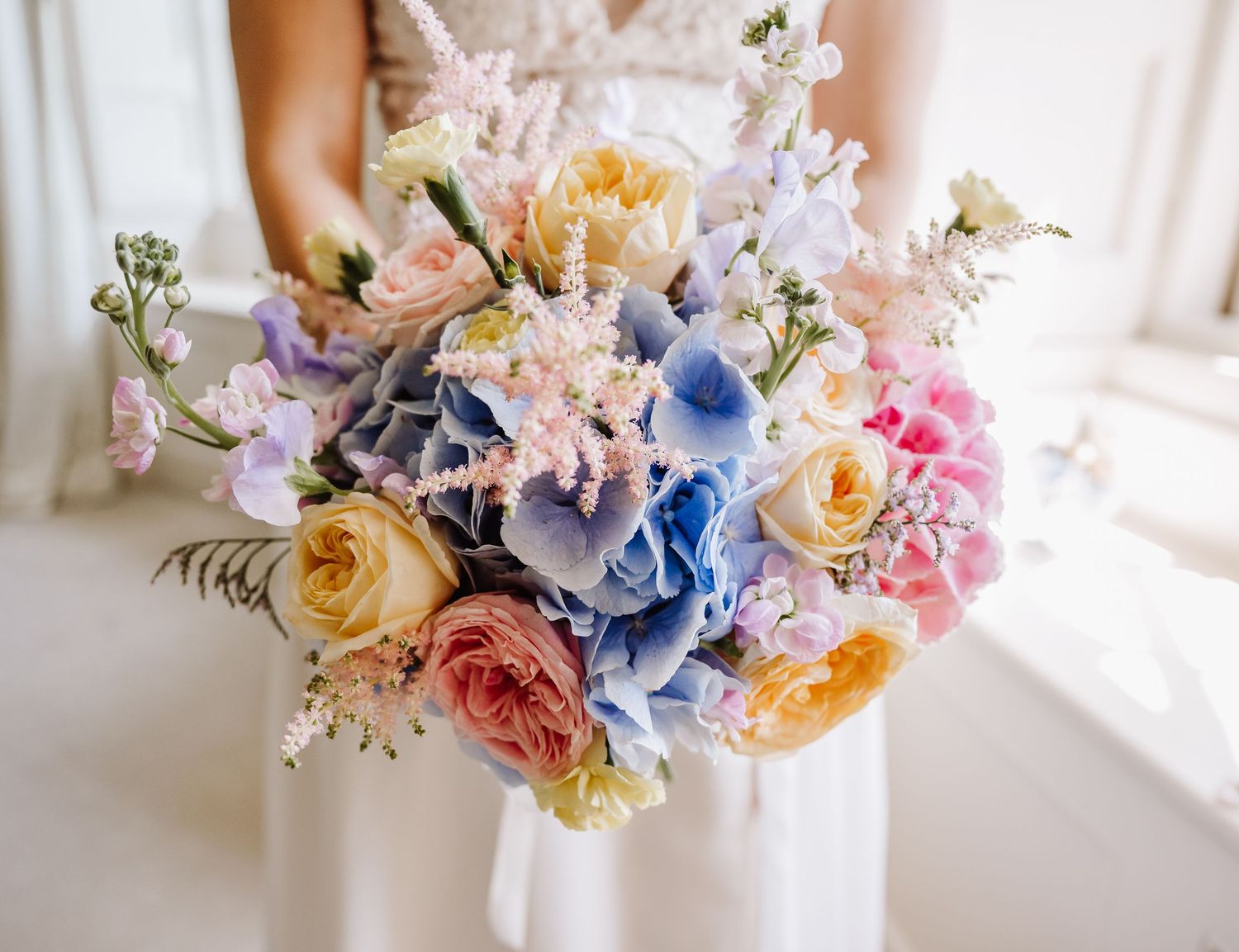 Bride holding a colorful wedding bouquet with blue hydrangeas, pink and yellow roses at Pennsylvania Castle, Portland Dorset
