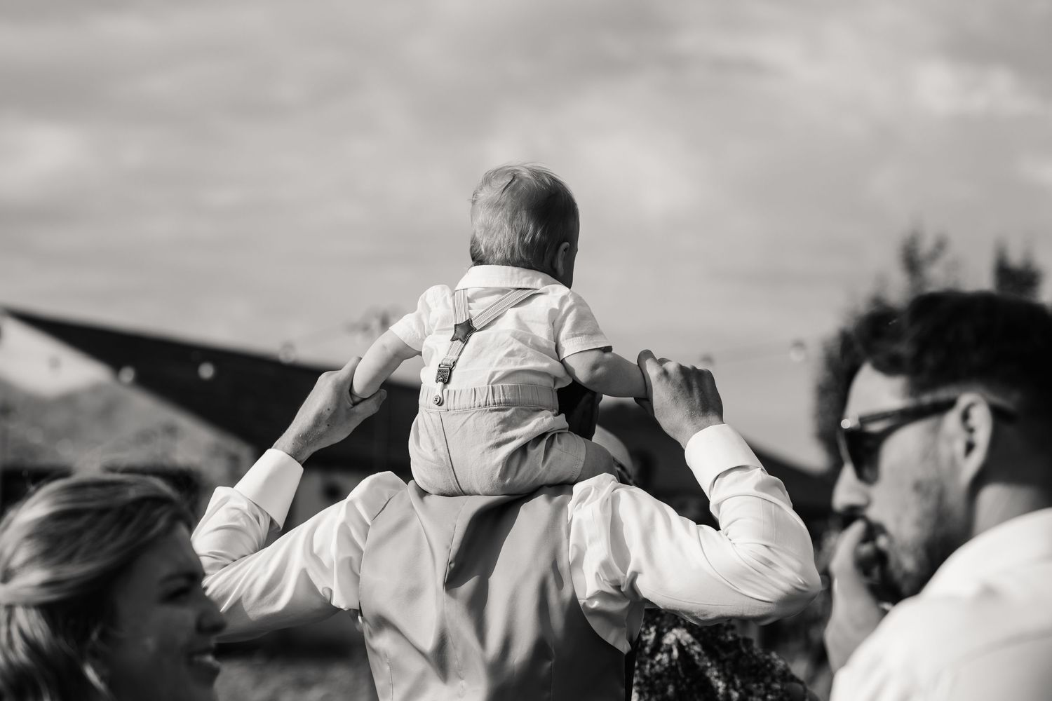 Black and white photo of parents lifting their baby up in the air outdoors.