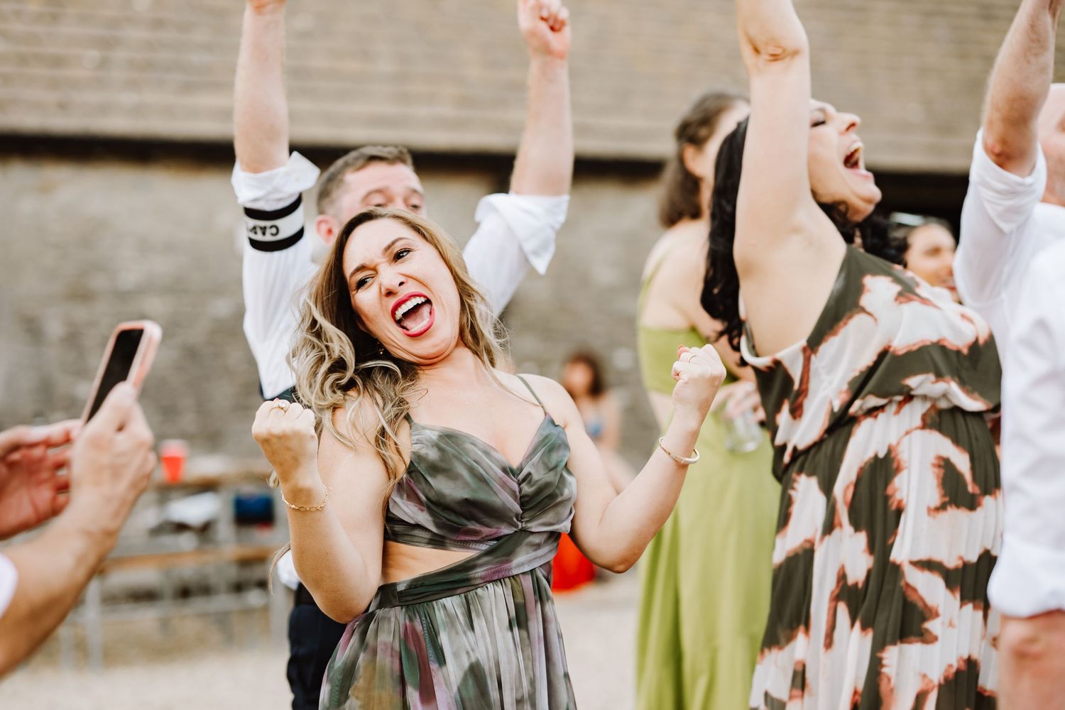 People celebrating with arms raised at an outdoor party, woman in green dress laughing joyfully.