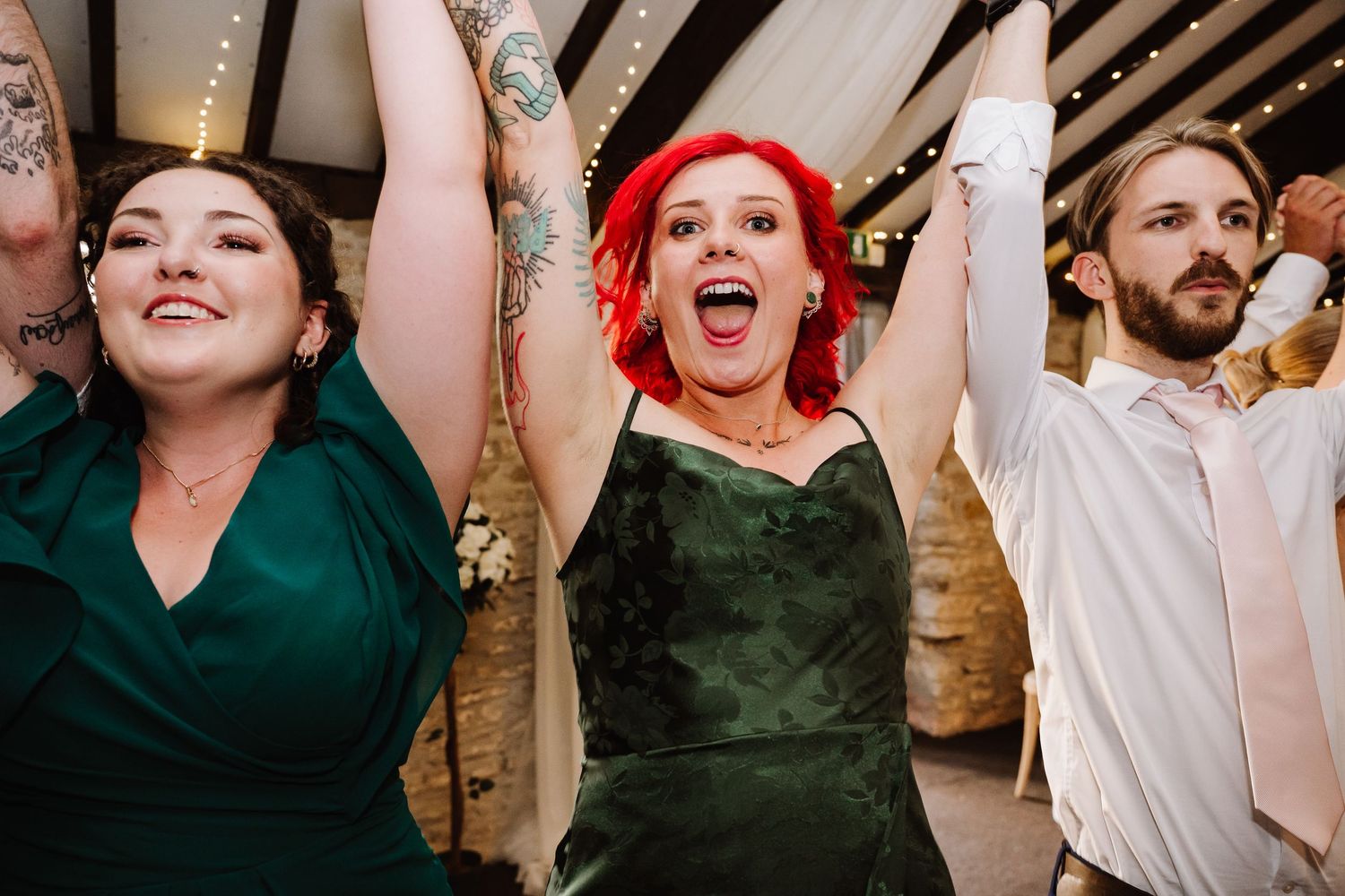 Guests dancing joyfully at a wedding reception, woman with red hair cheering with arms raised.