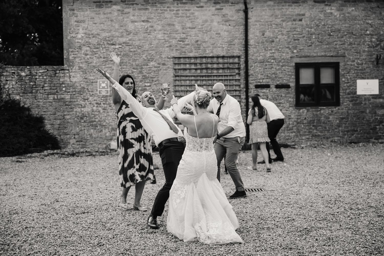 Bride and wedding guests celebrate joyfully outdoors at a rustic barn wedding venue in black and white.