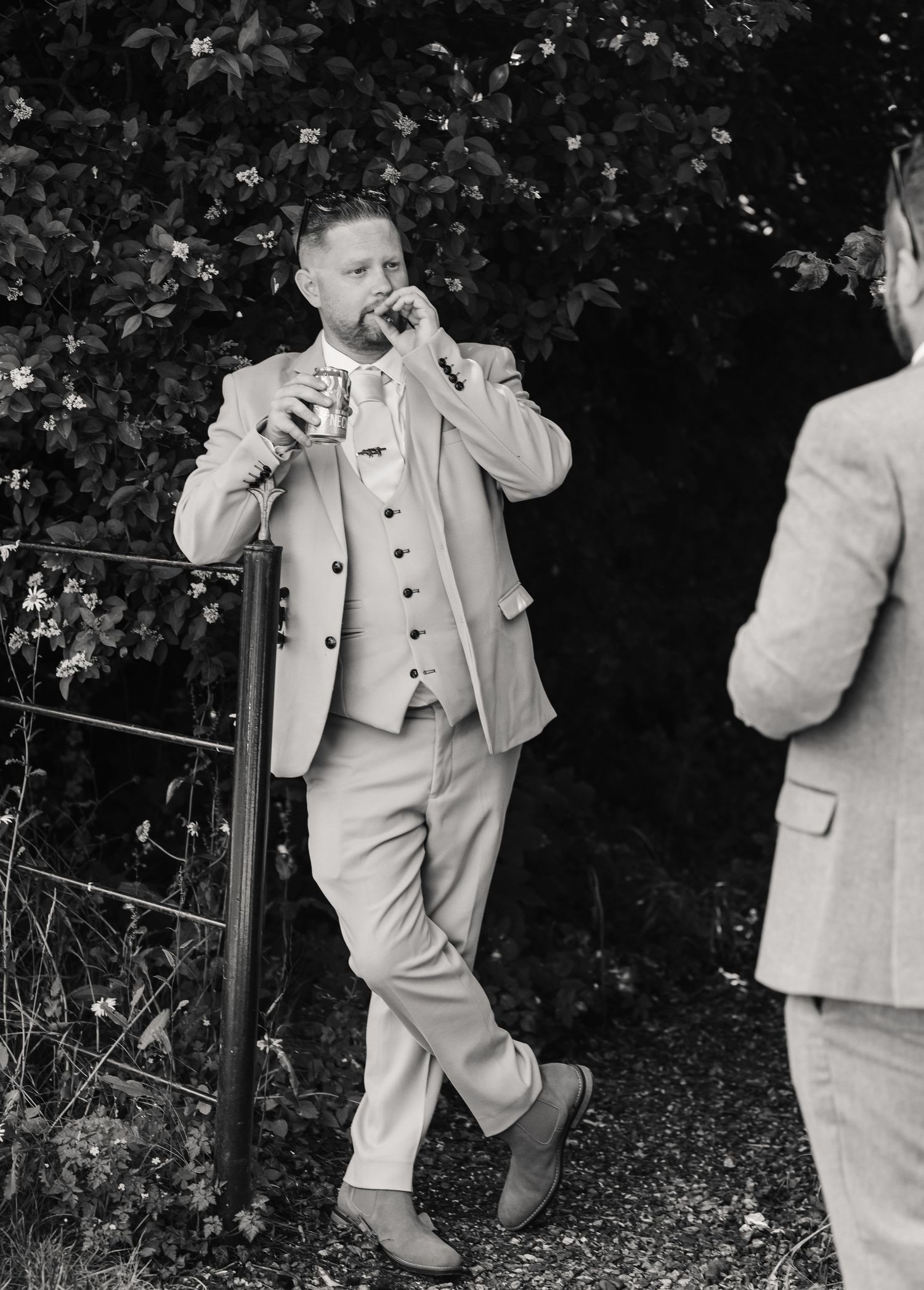 Groom in a light grey three-piece suit drinking and smoking outdoors before wedding ceremony at Elmhay, Orchardleigh estate, Frome