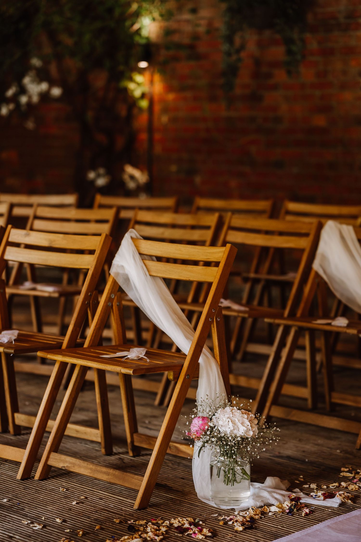 Wooden folding chairs decorated with white fabric and floral arrangements at an indoor wedding ceremony at Elmhay, Orchardleigh estate, From