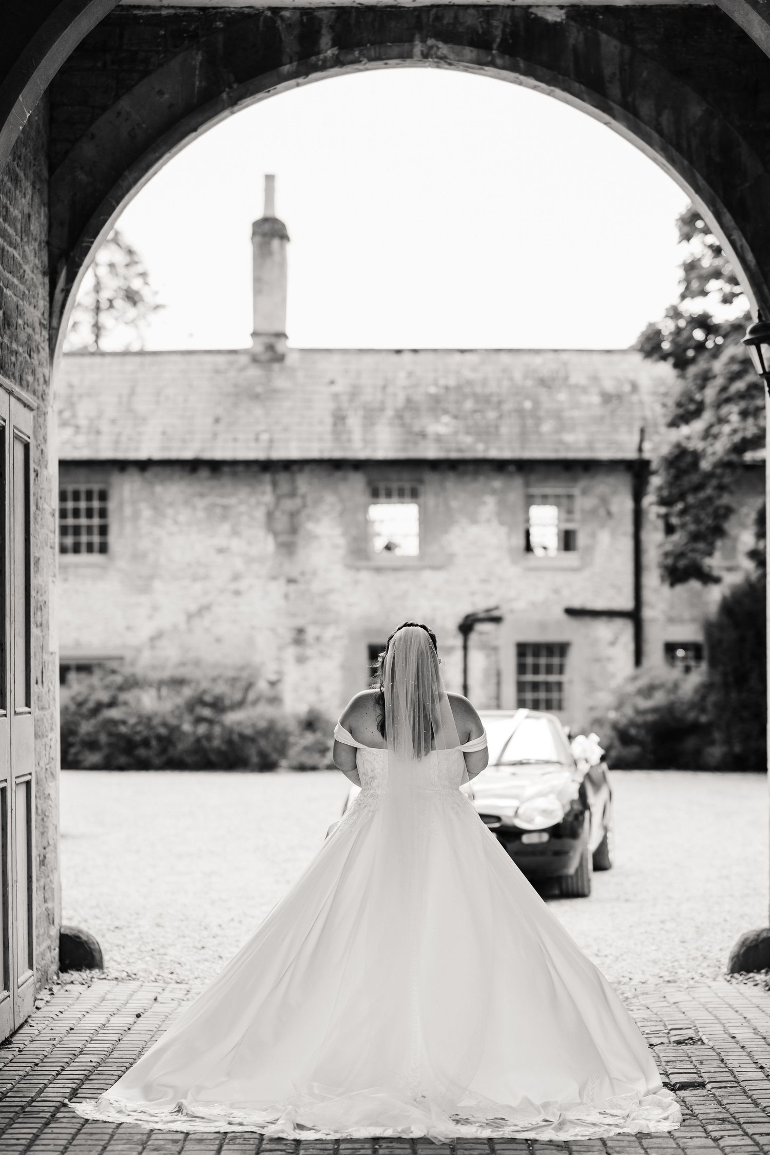 Bride in a ball gown wedding dress viewed through an archway at a historic stone venue at Elmhay, Orchardleigh estate, Frome