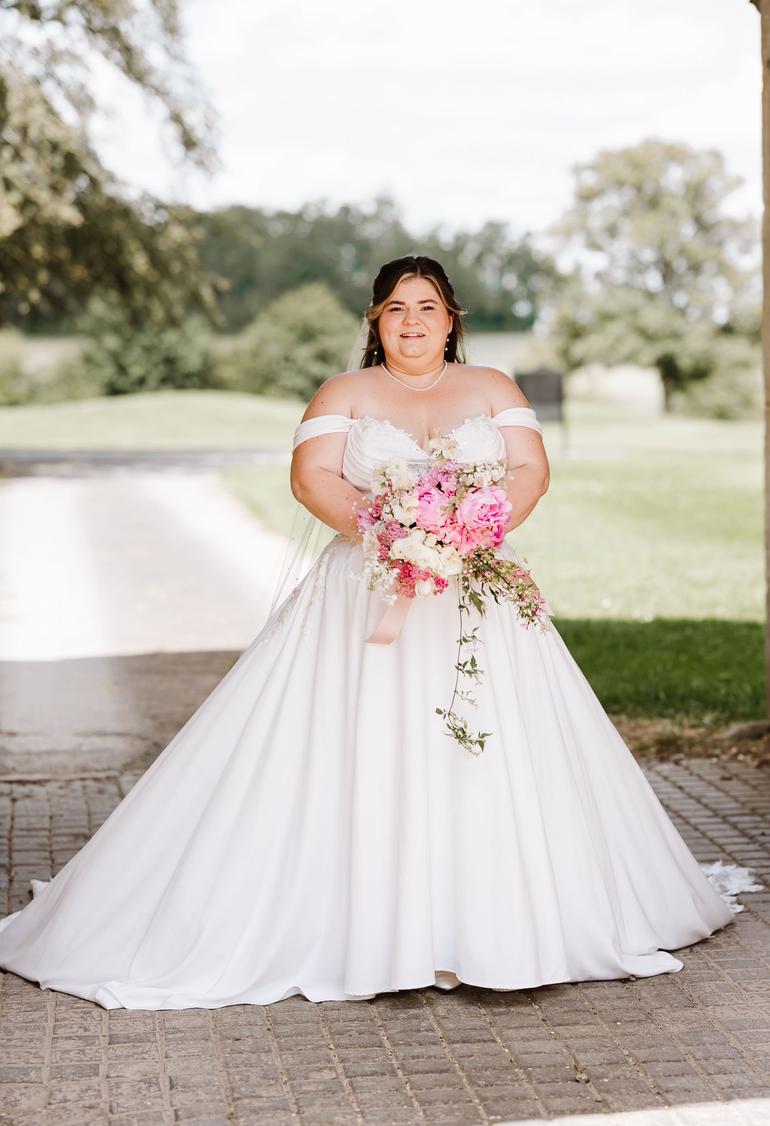 Bride in an off-shoulder ball gown holding a cascading pink and white bouquet outdoors at Elmhay, Orchardleigh estate, Frome