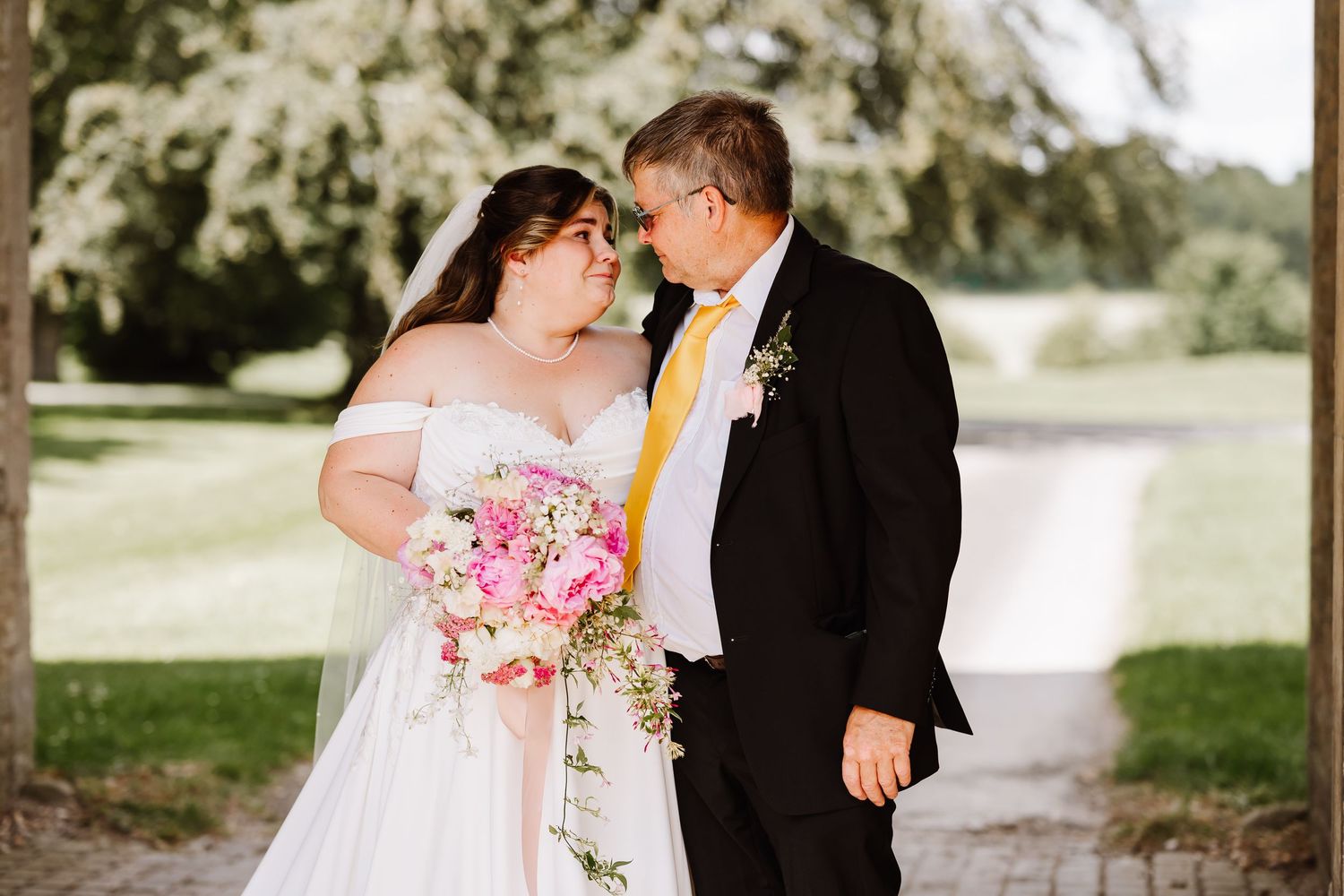 Bride and groom sharing a romantic moment under trees with pink cascading bouquet outdoors at Elmhay, Orchardleigh estate, Frome