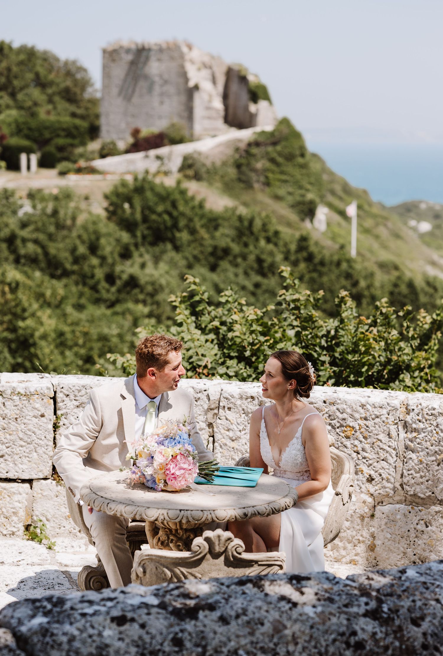 Newlyweds sitting at a stone table with colorful bouquet overlooking at Pennsylvania Castle, Portland Dorset