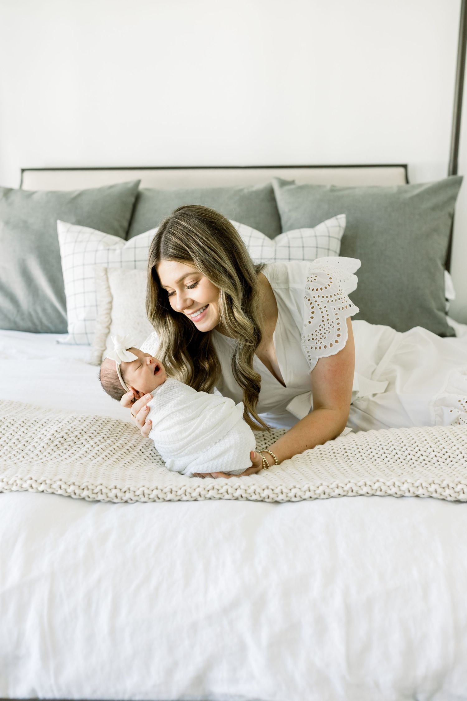 Sweet moment between parent and newborn baby lying together on white bedding with grey pillows.