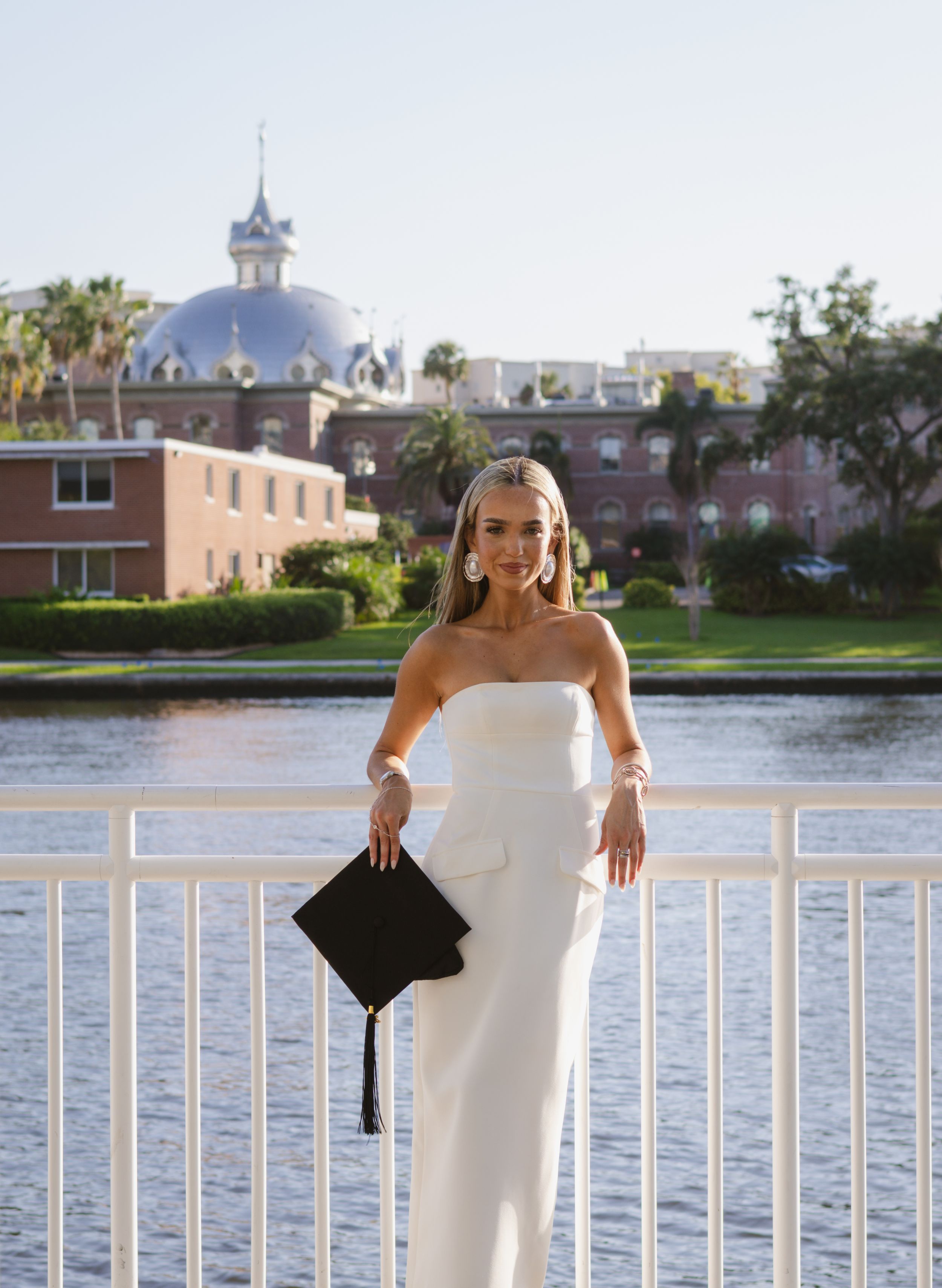 A girl holding her graduation cap in front of the University of Tampa.