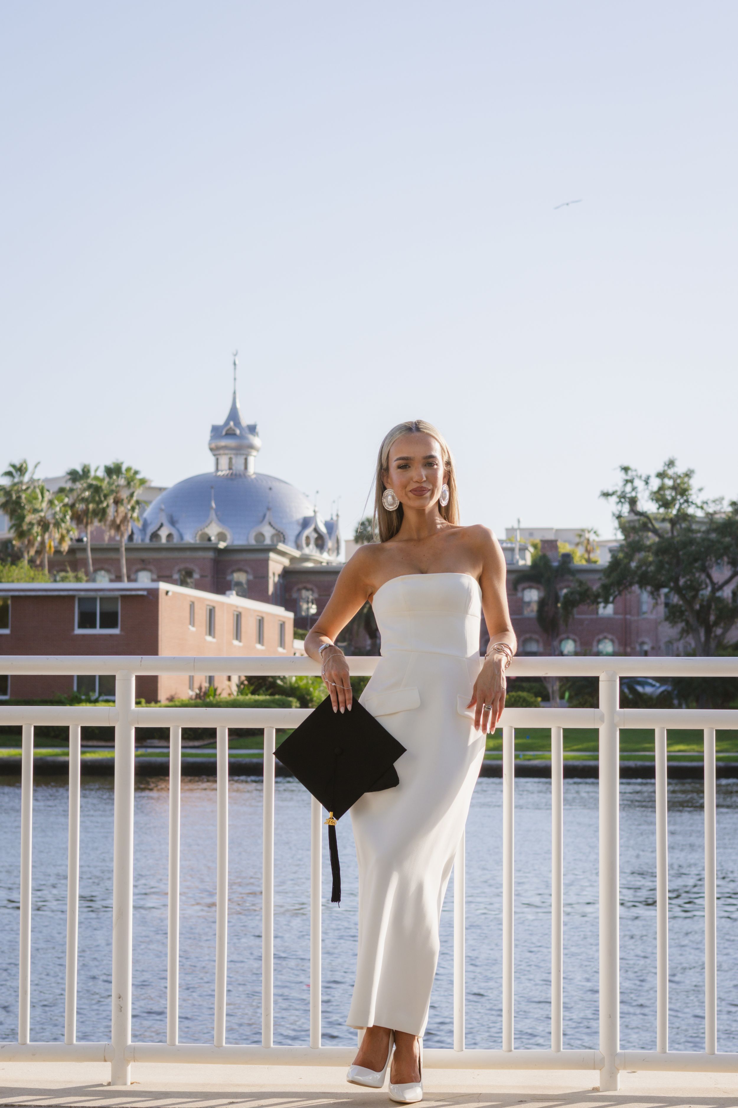 A girl in a white dress is leaned against the railings of Curtis Hixon park, in Tampa, FL.