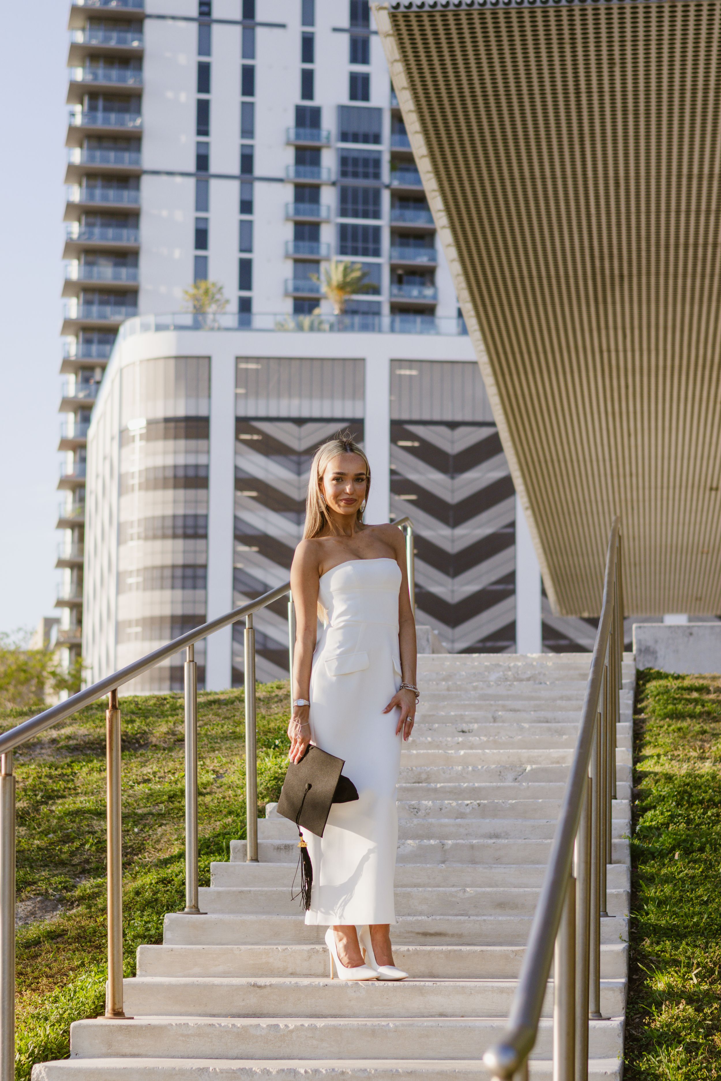 In downtown Tampa, a girl on the stairs holds her graduation cap.