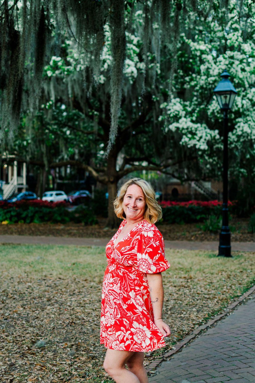 A red and white floral dress stands out against a backdrop of Spanish moss and oak trees in a Southern park setting.