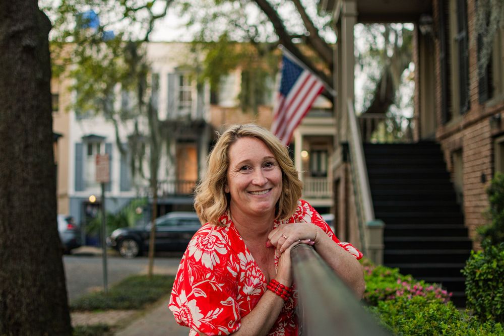 Leaning on a railing in a historic neighborhood with Spanish moss and an American flag in view.