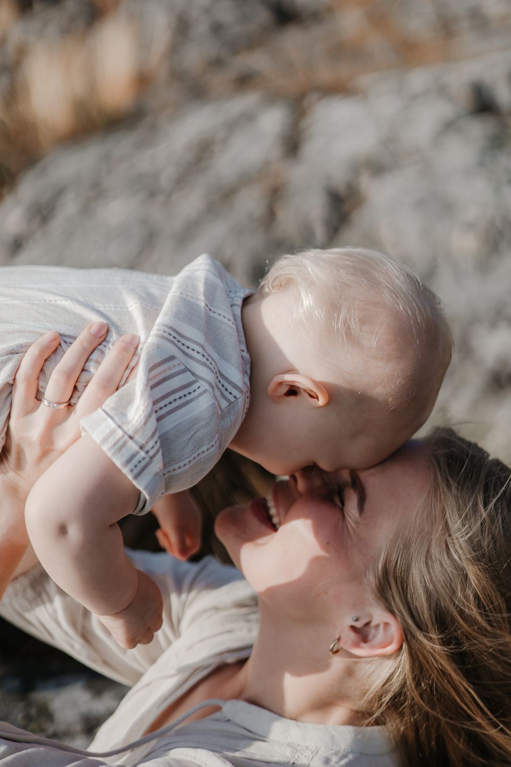 A tender moment between parent and baby on rocky coastal terrain.
