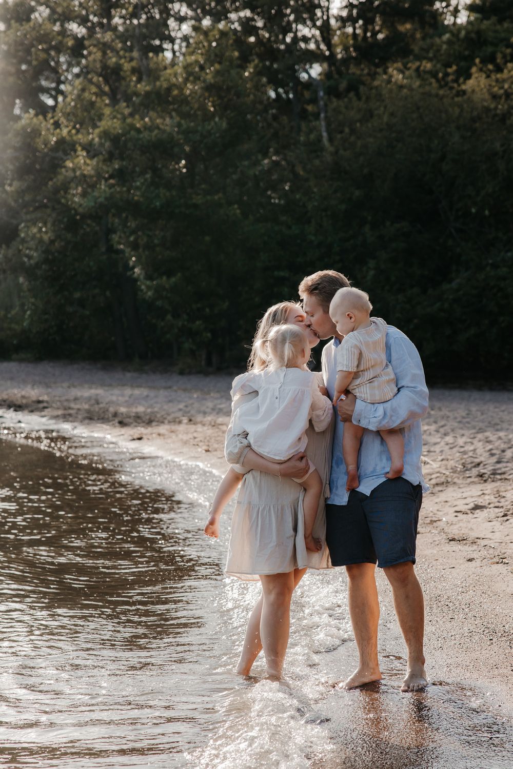 A family stands ankle-deep in water at the beach during golden hour.