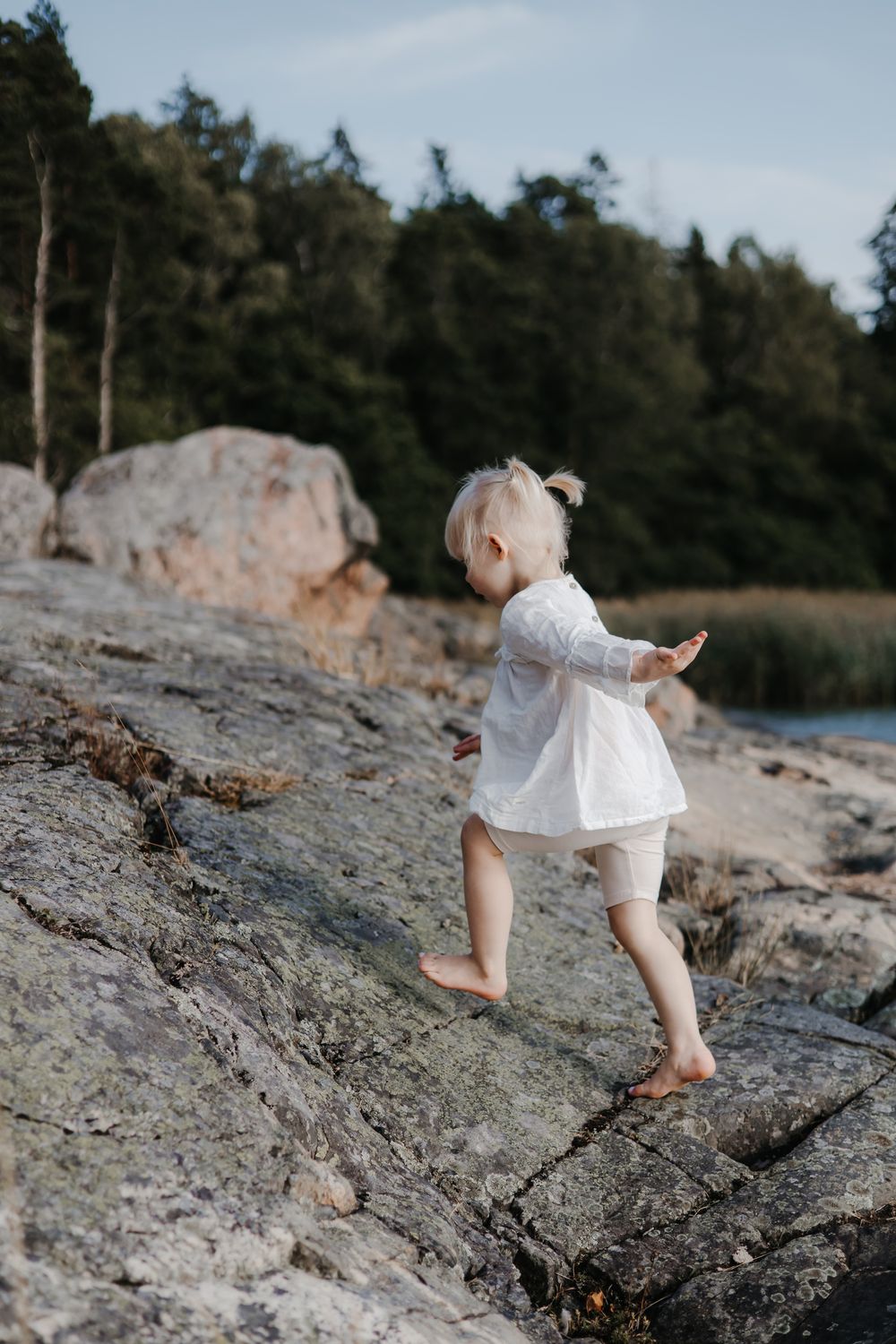 A small child in white clothing climbing on rocky coastal terrain.