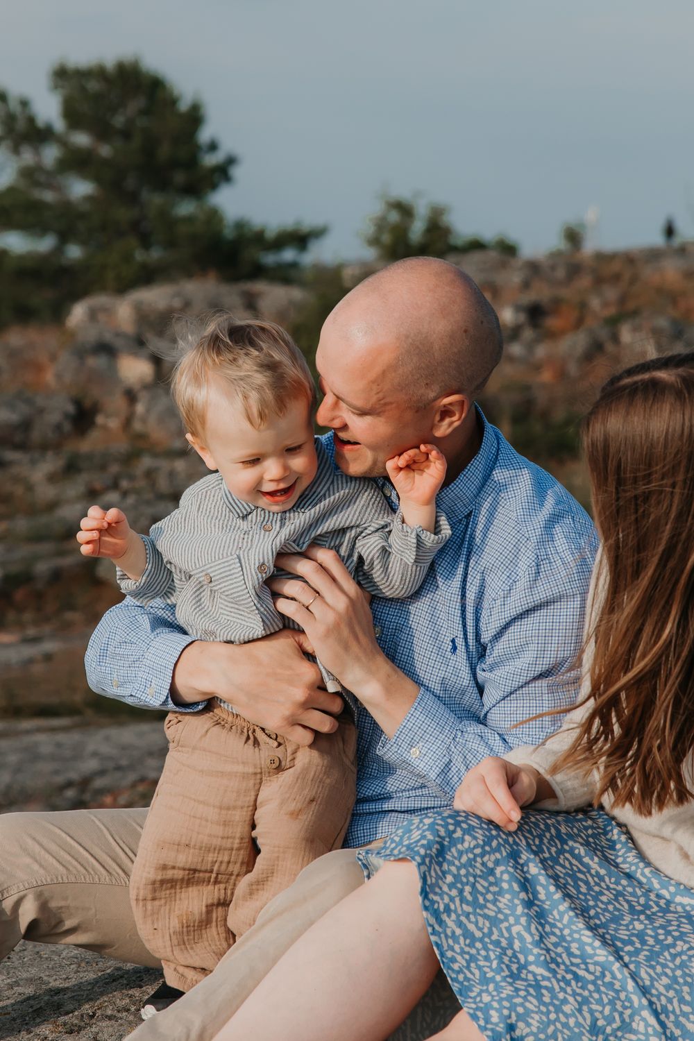 A joyful moment shared between family members sitting on coastal rocks.