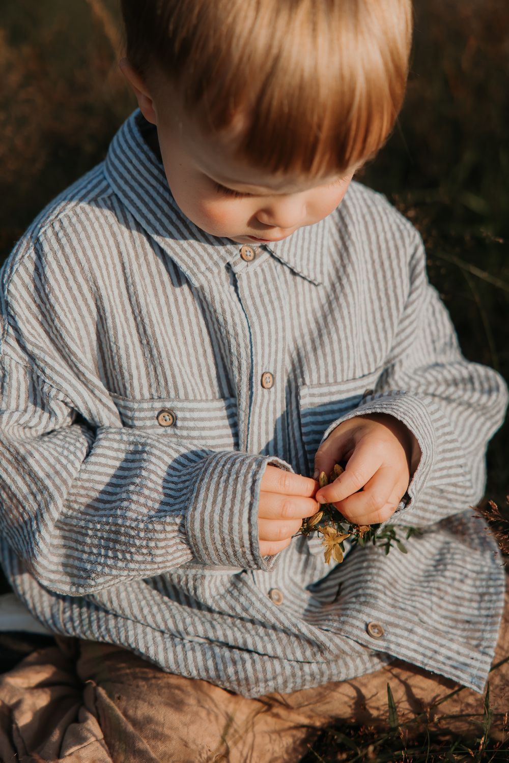 Close-up of small hands in striped clothing examining something delicate in natural lighting.