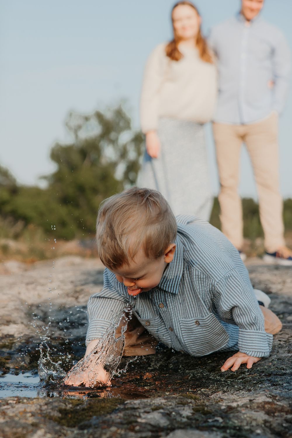 Child in blue checkered shirt playing and splashing in shallow water.