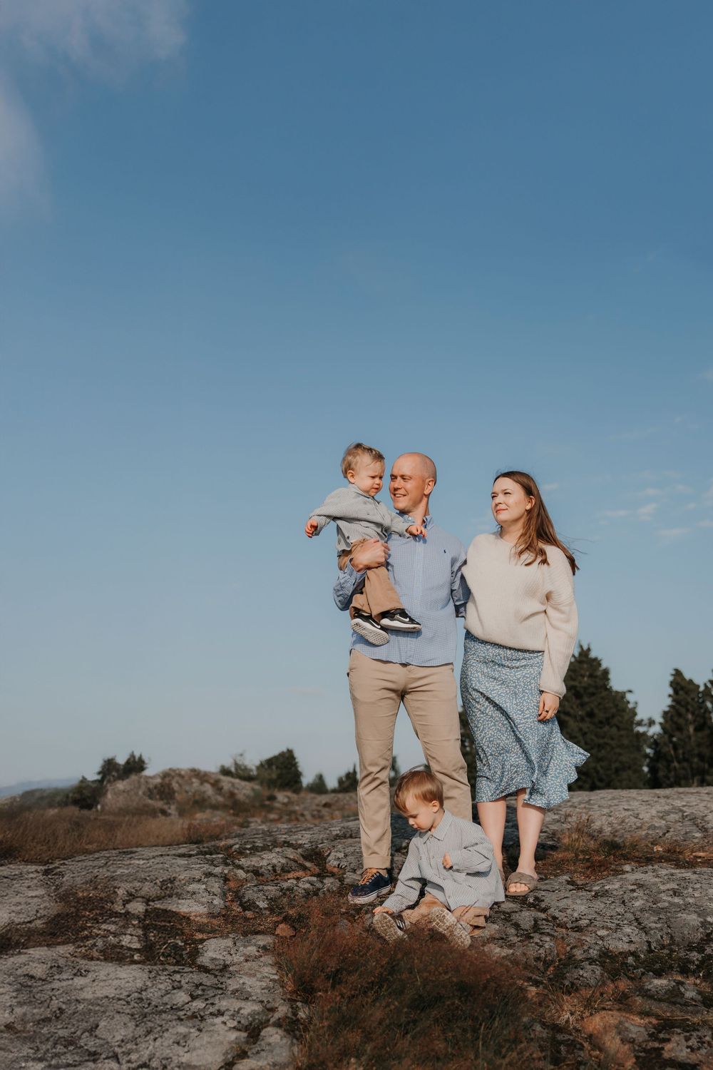 A family poses together on a rocky cliff overlooking the ocean on a sunny day.