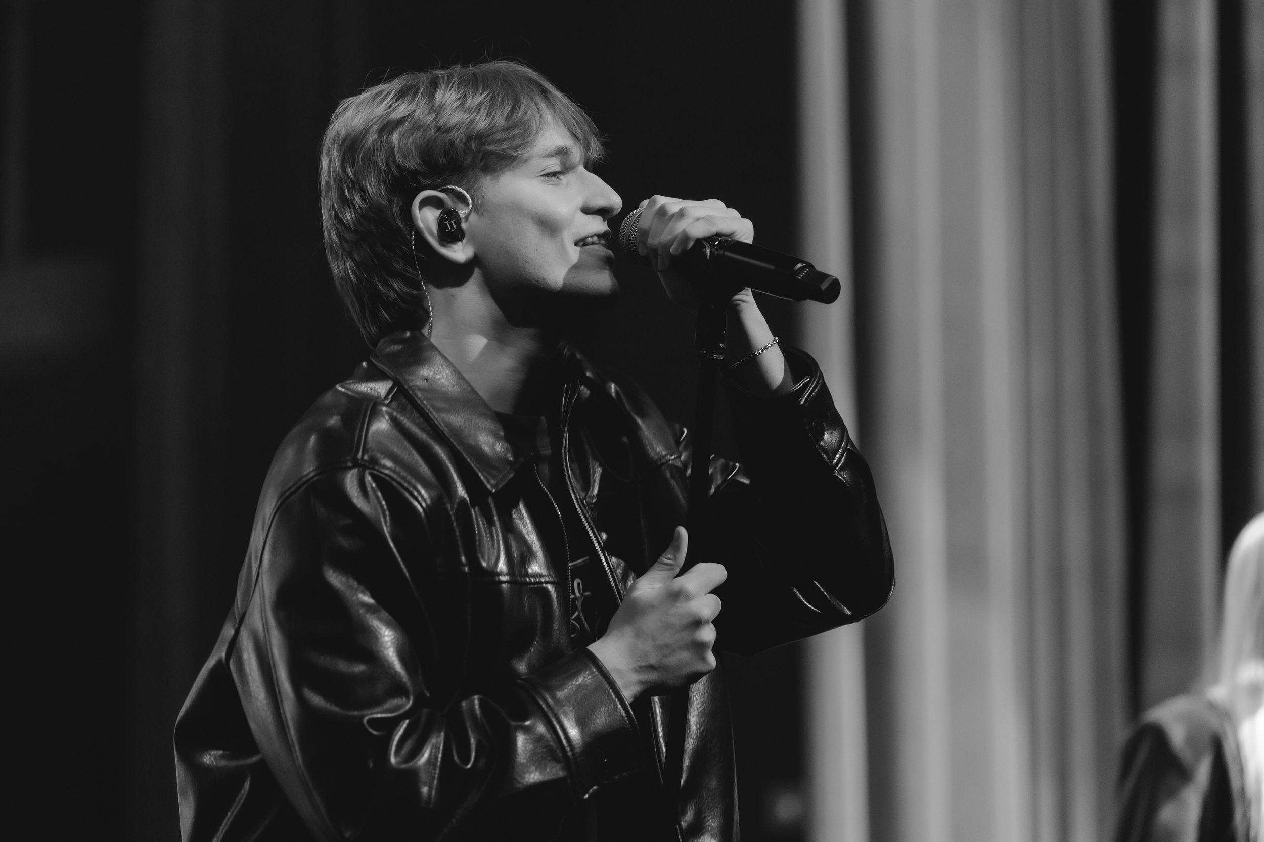 Performer in a leather jacket sings passionately into a microphone during a live concert performance.