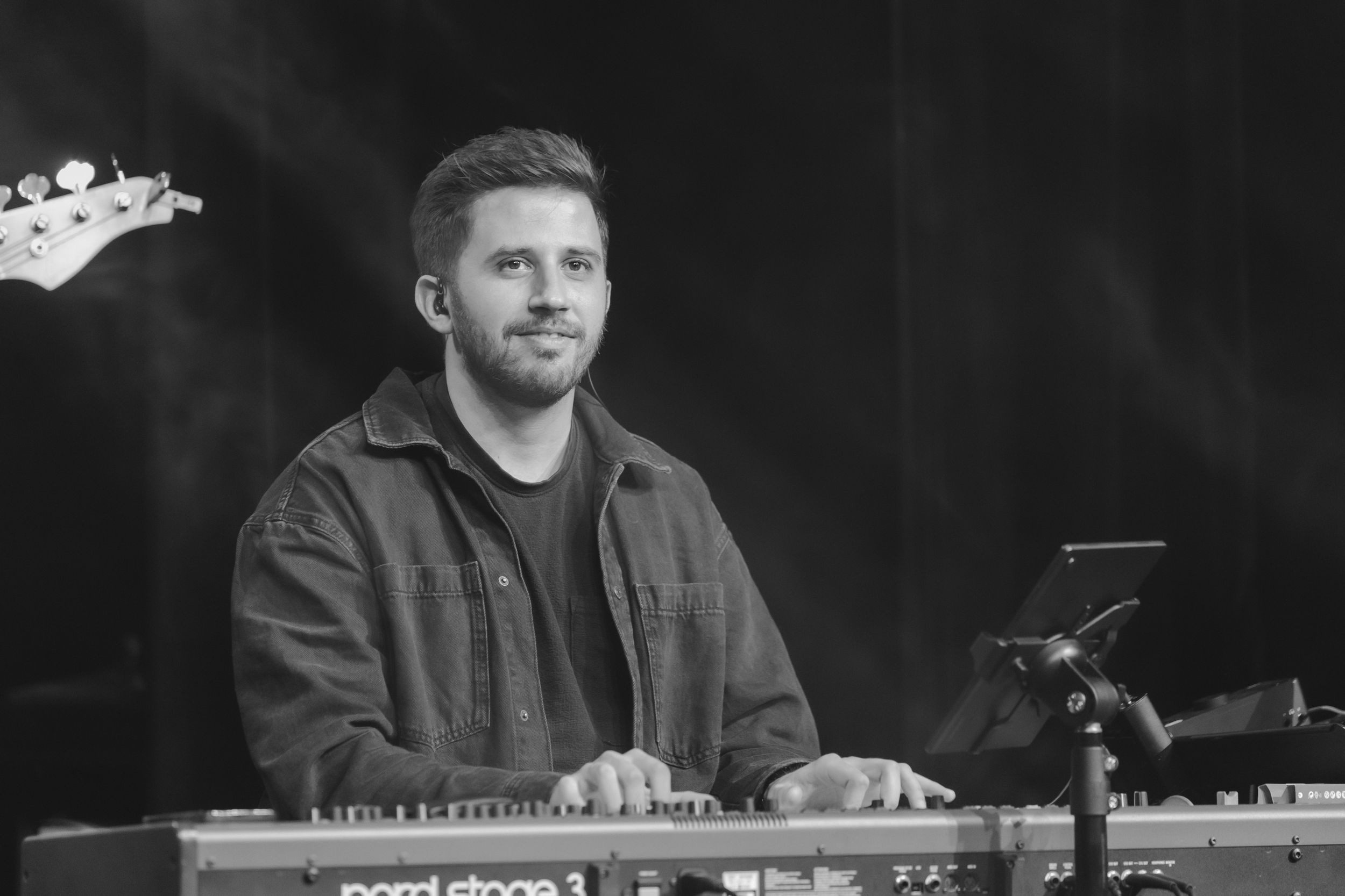 Musicians perform on stage with keyboards and electronic equipment during a live performance in black and white.