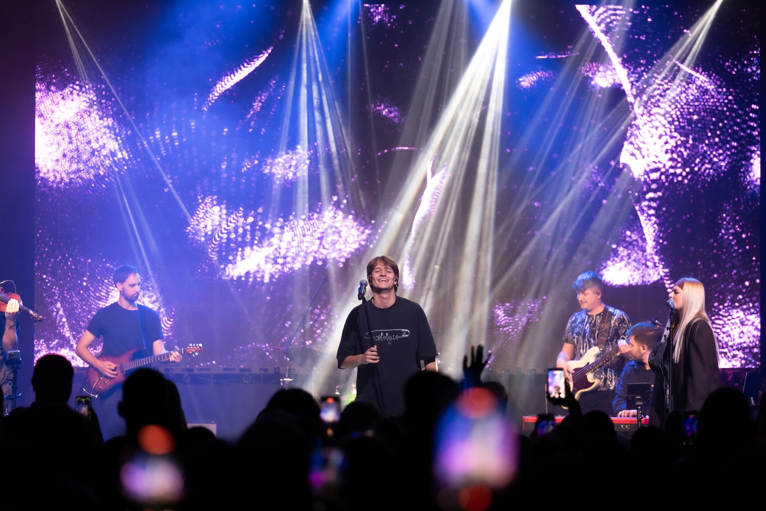 Concert performers on stage illuminated by dramatic blue and purple lighting effects during a live music performance.
