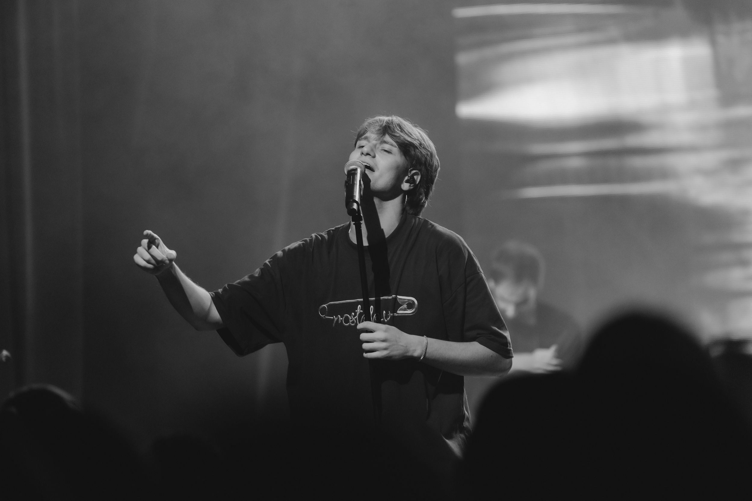A performer sings passionately on stage during a concert in dramatic black and white lighting.