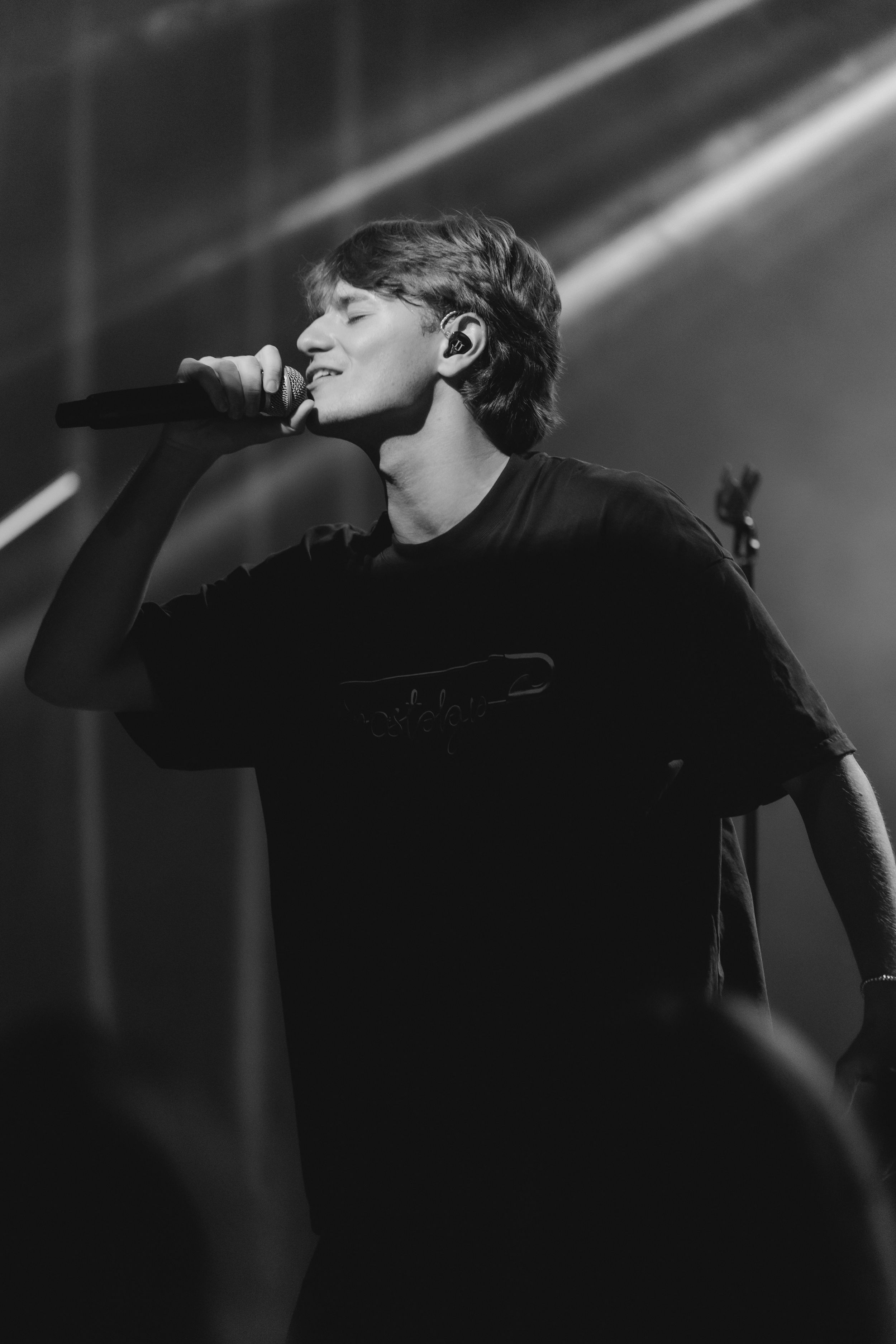 A dramatic black and white performance photo showing a silhouetted figure singing on stage with dramatic lighting beams.