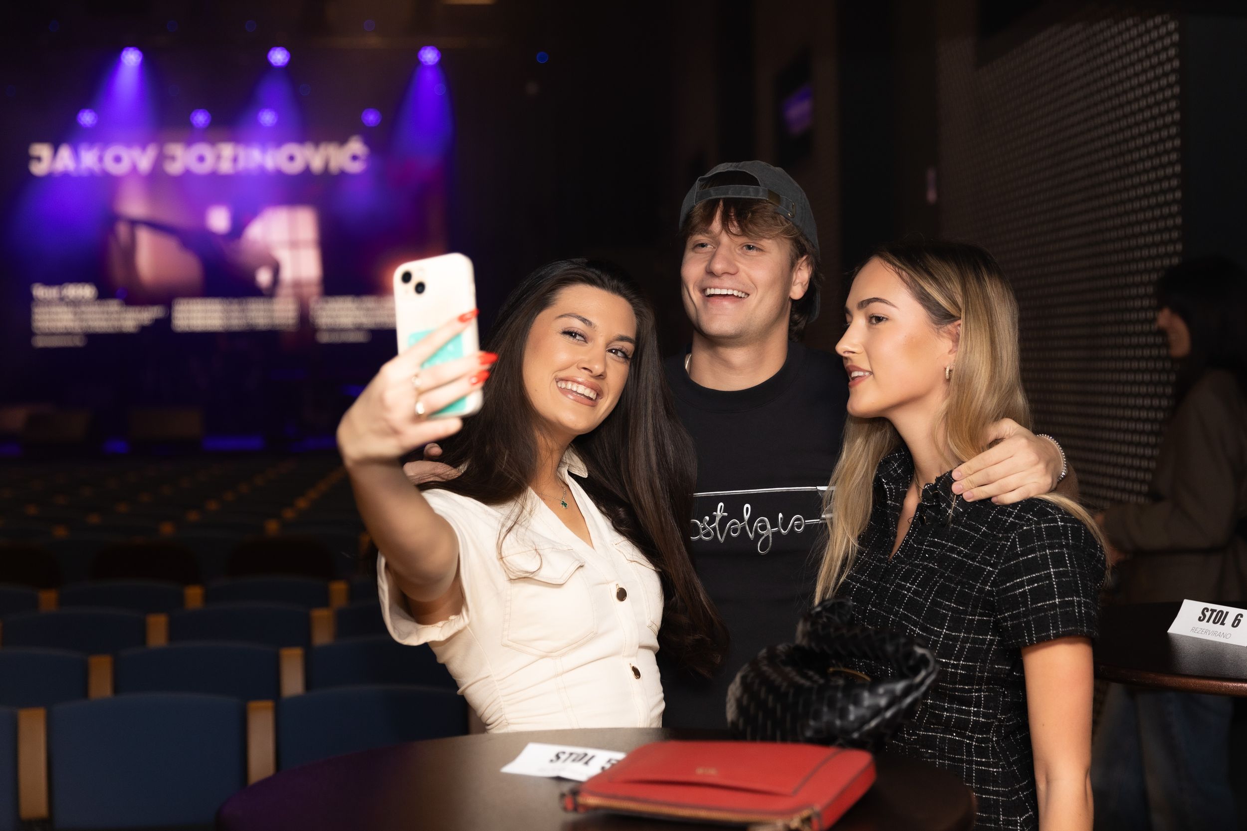 People taking selfies and enjoying themselves at a dimly lit nightclub or bar with purple lighting.