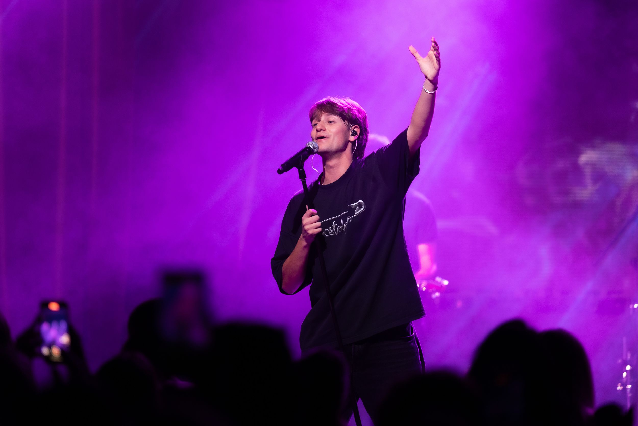 Concert performer on stage with dramatic purple lighting and fog effects during live music performance.