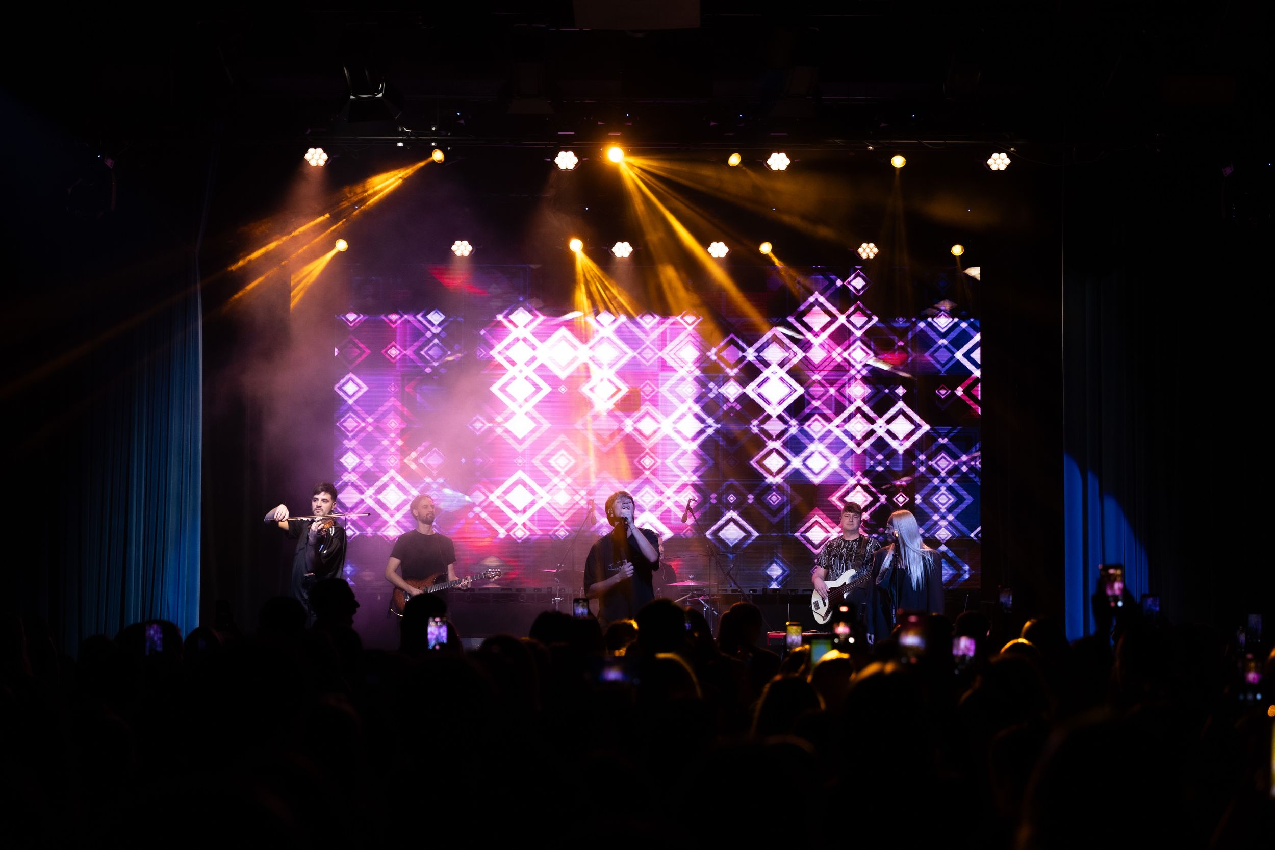Concert stage illuminated with vibrant purple and orange lights creating a dramatic silhouette of performers.