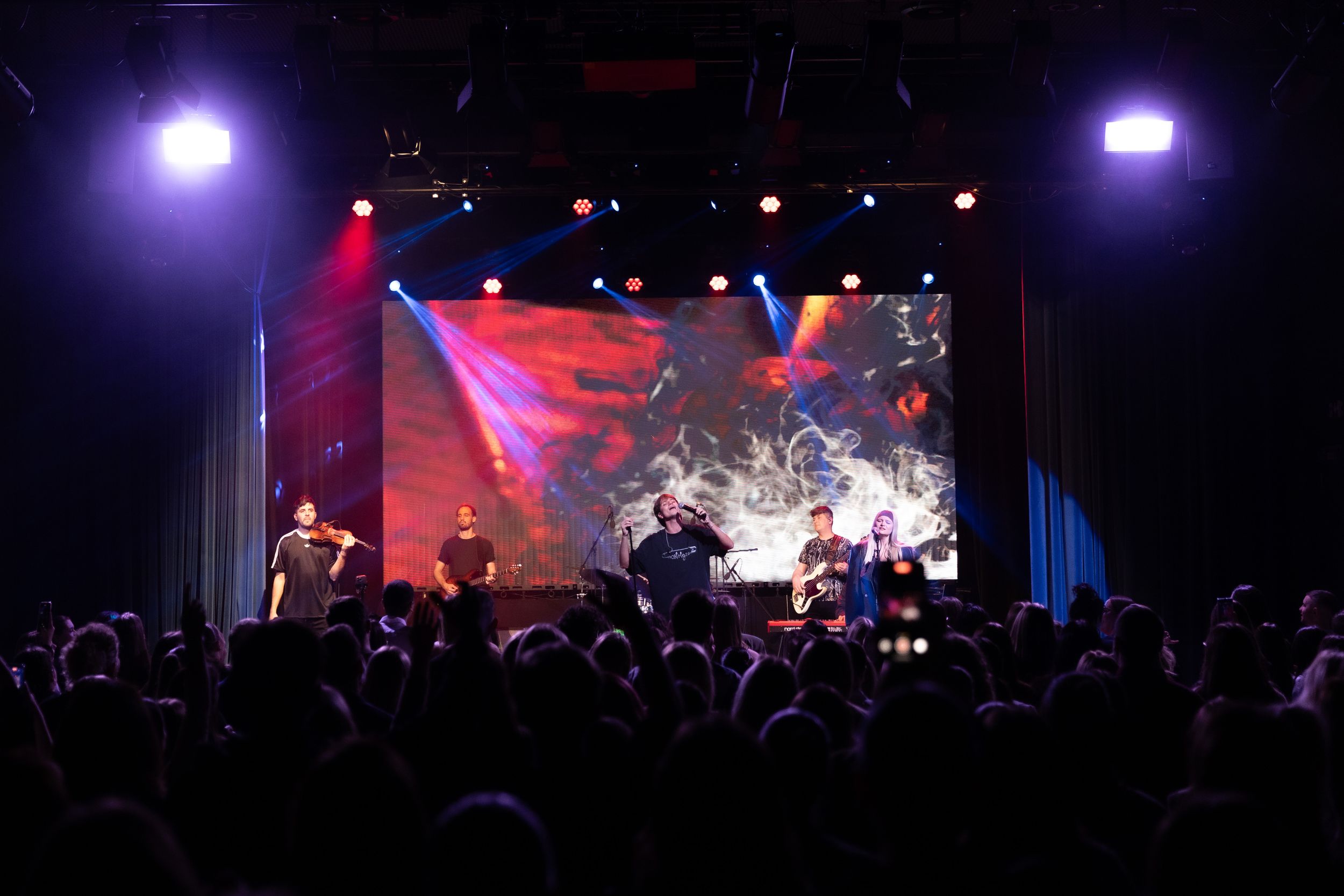 Concert performers on stage with dramatic purple and red lighting effects illuminating the crowd below.