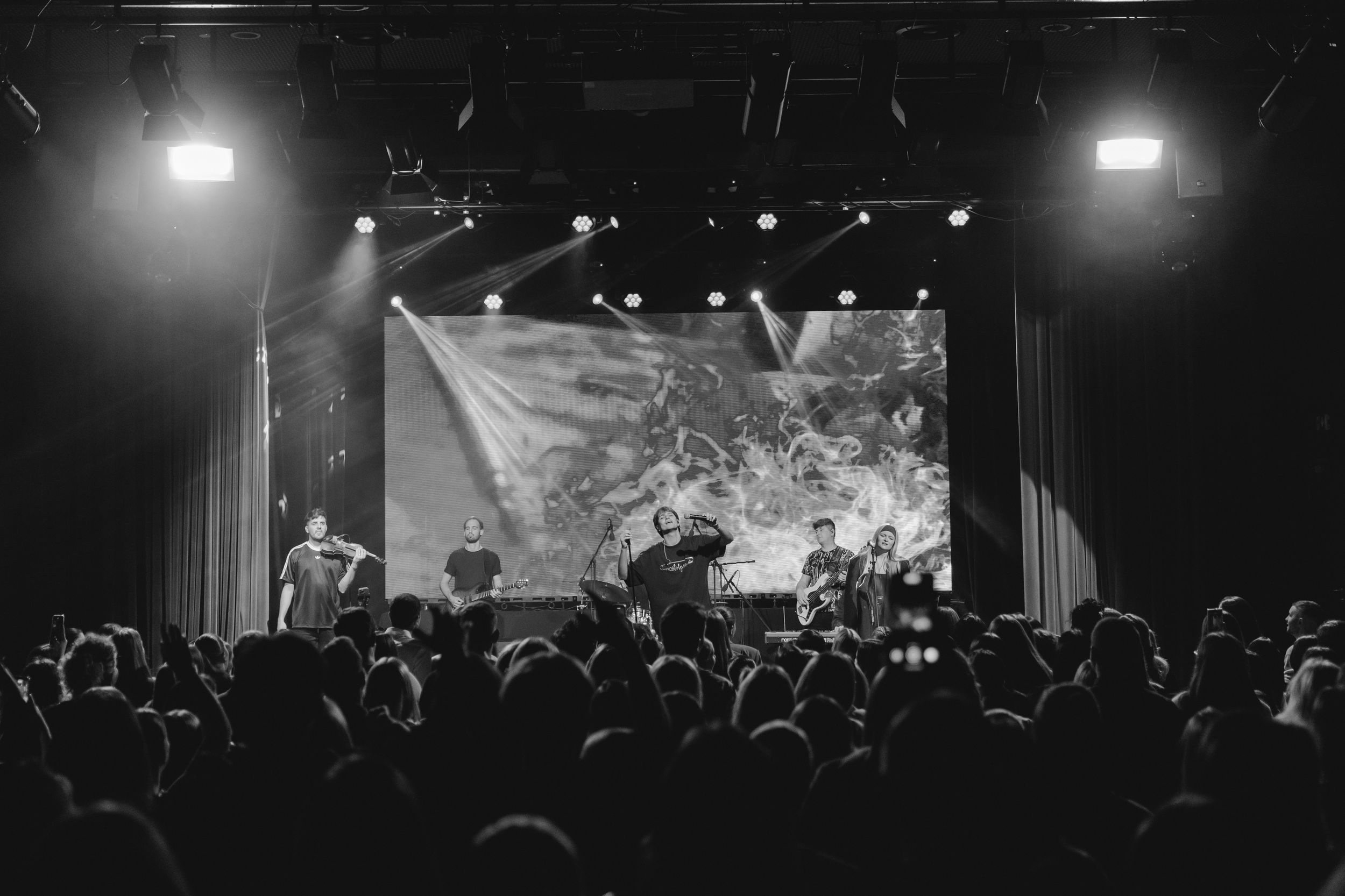 Black and white concert photos showing silhouettes of performers on stage with dramatic lighting and crowd in background.