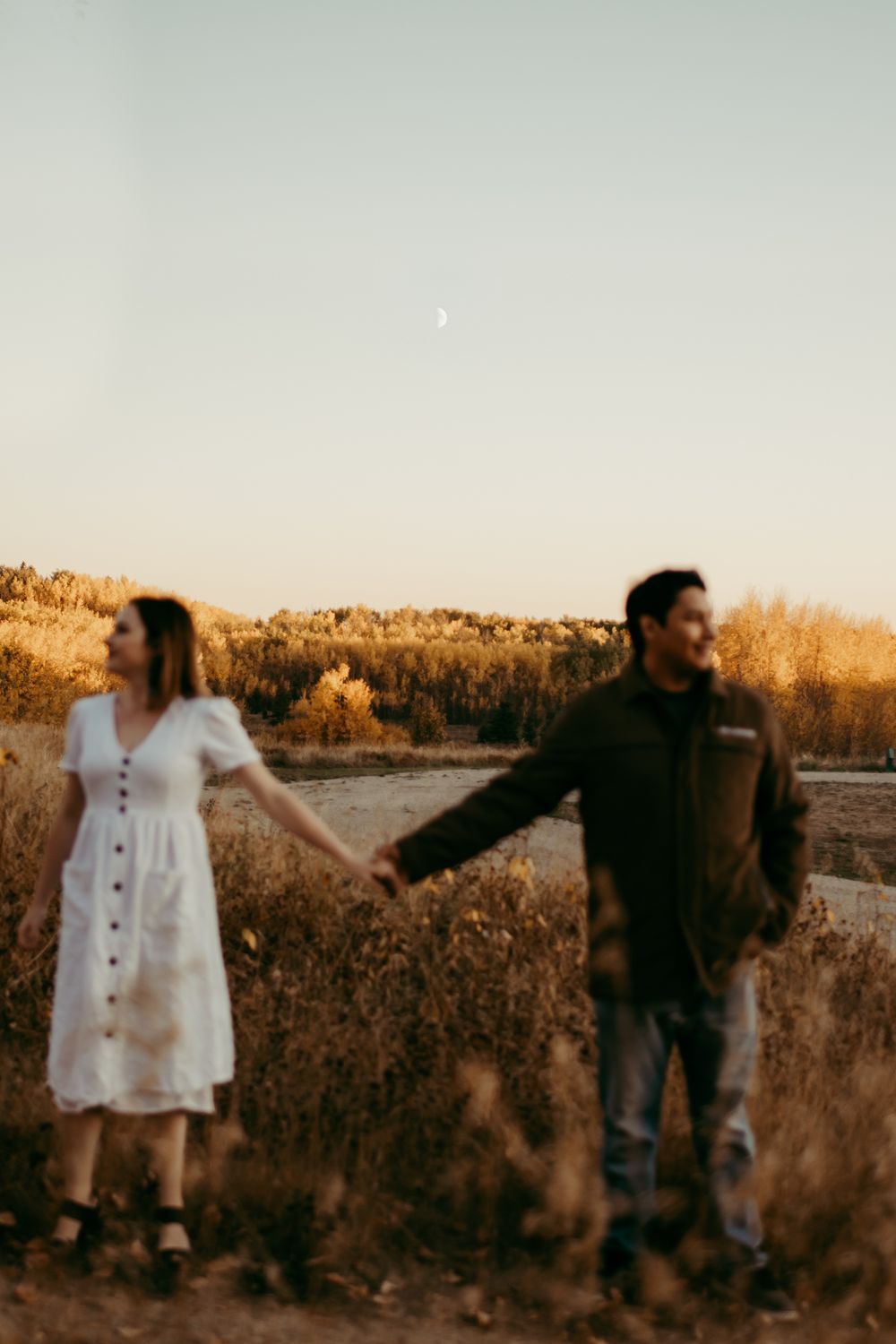 Couple holding hands at sunset in field with dreamy golden light.