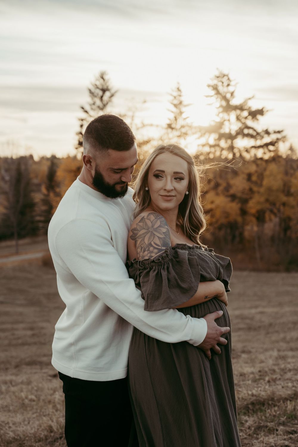 A couple embraces outdoors at sunset with golden autumn trees in the background during a photo session.