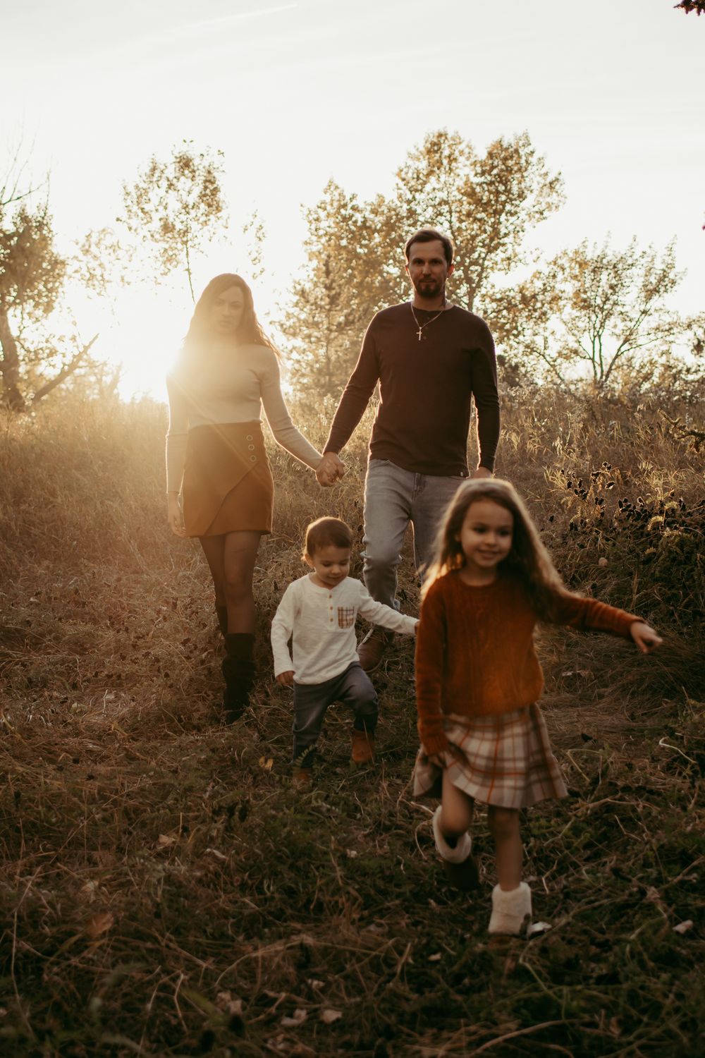 Family walking together at sunset through golden field with children running ahead.