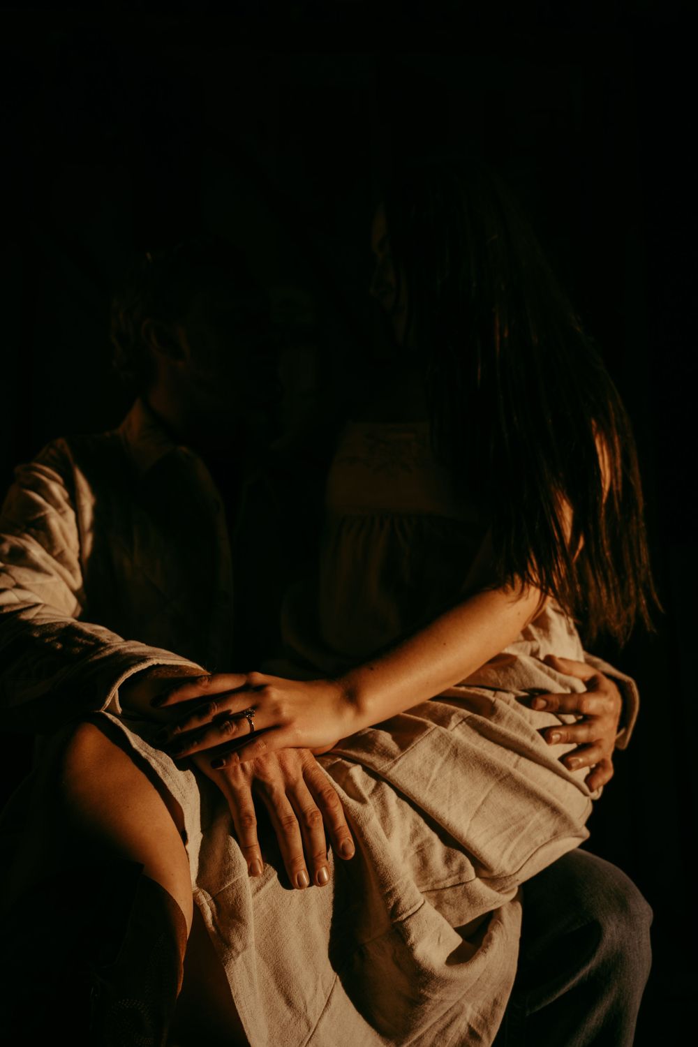 Intimate low-light artistic photograph showing embracing hands.