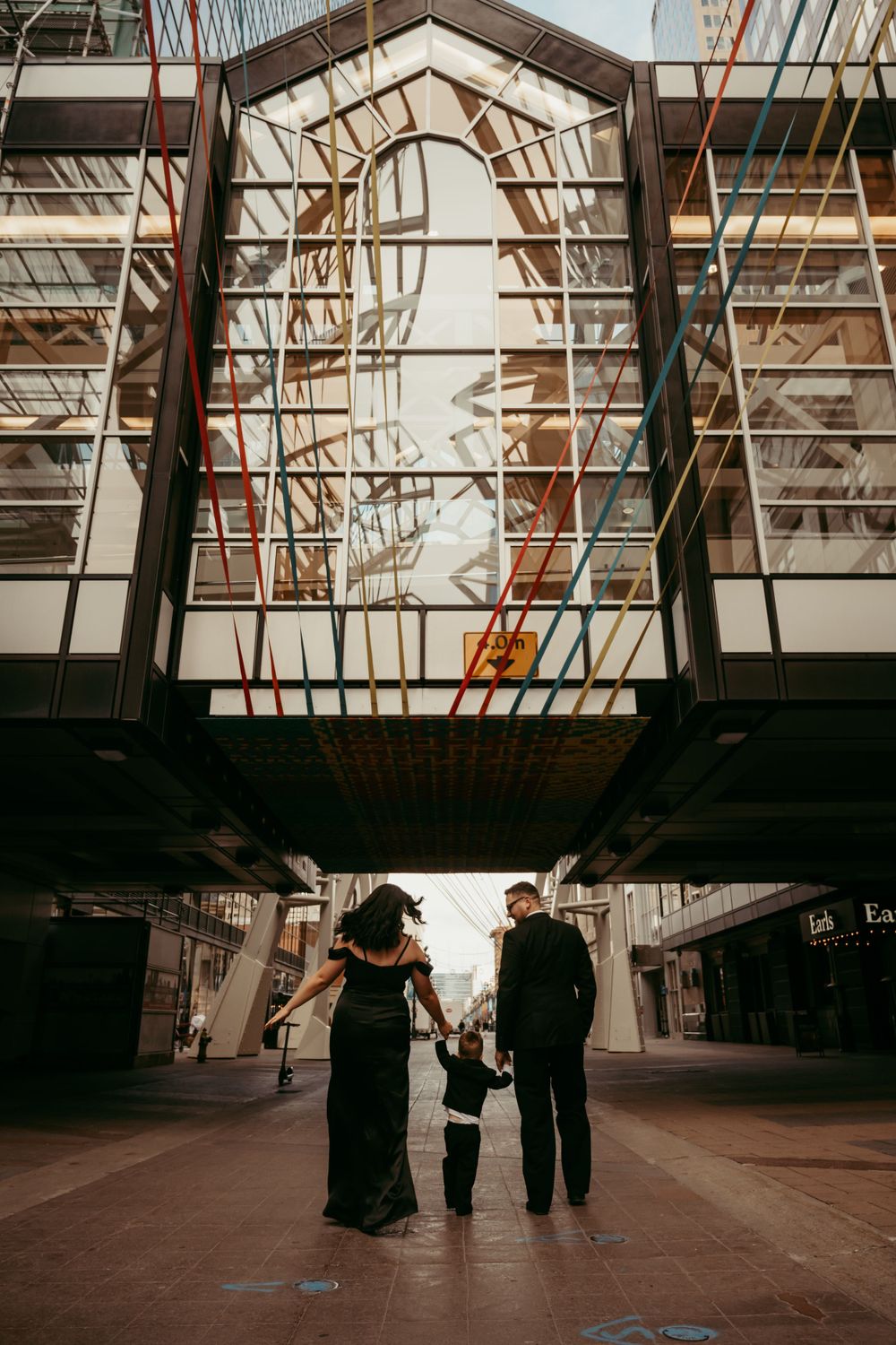 Three figures silhouetted under an urban bridge walkway with architectural arches and metal framework above.