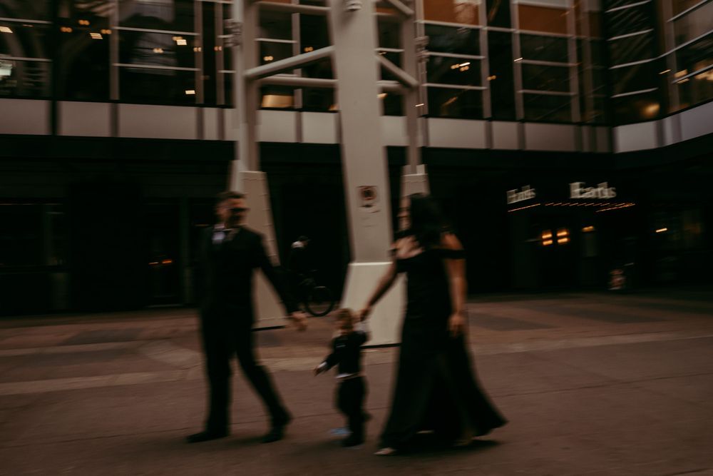 A silhouetted family holds hands while walking together in an urban plaza at dusk.