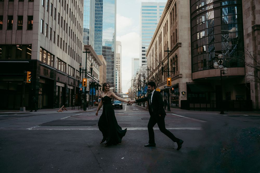 Two pedestrians cross an empty downtown street between tall buildings on a moody urban day.