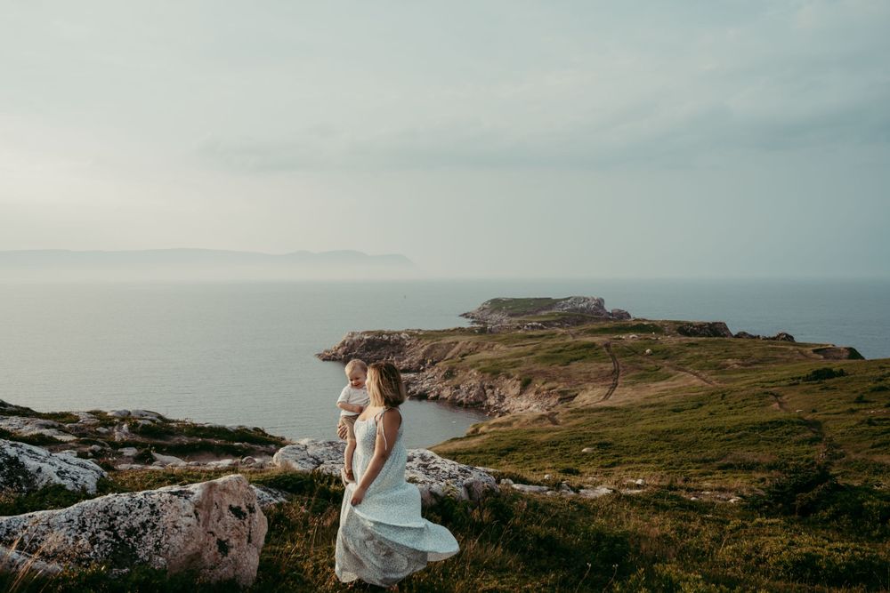 Wedding dress flowing in wind as figure stands on dramatic coastal cliffs overlooking ocean.