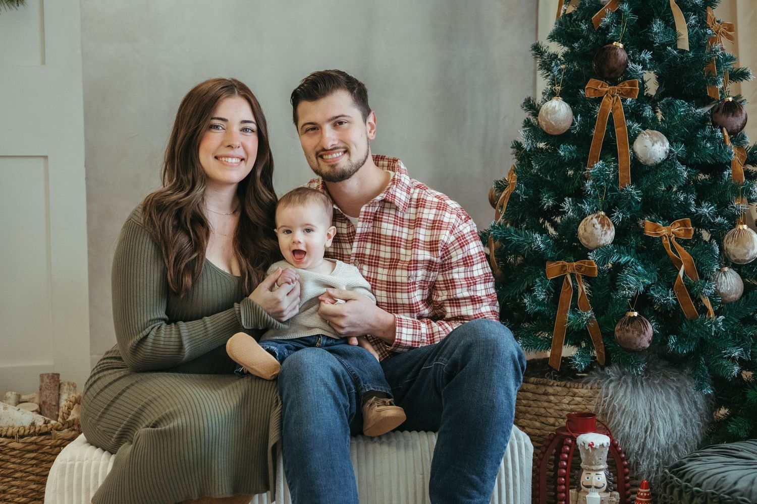 Family poses for cozy holiday photos near decorated Christmas tree in living room.