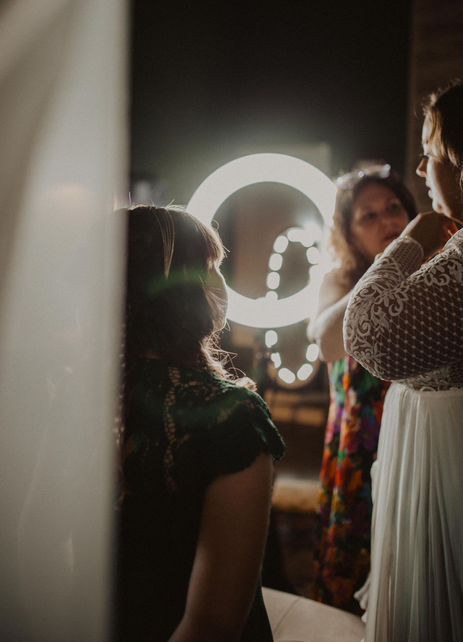 Wedding preparations in a moody indoor setting with dramatic lighting and white gown details.