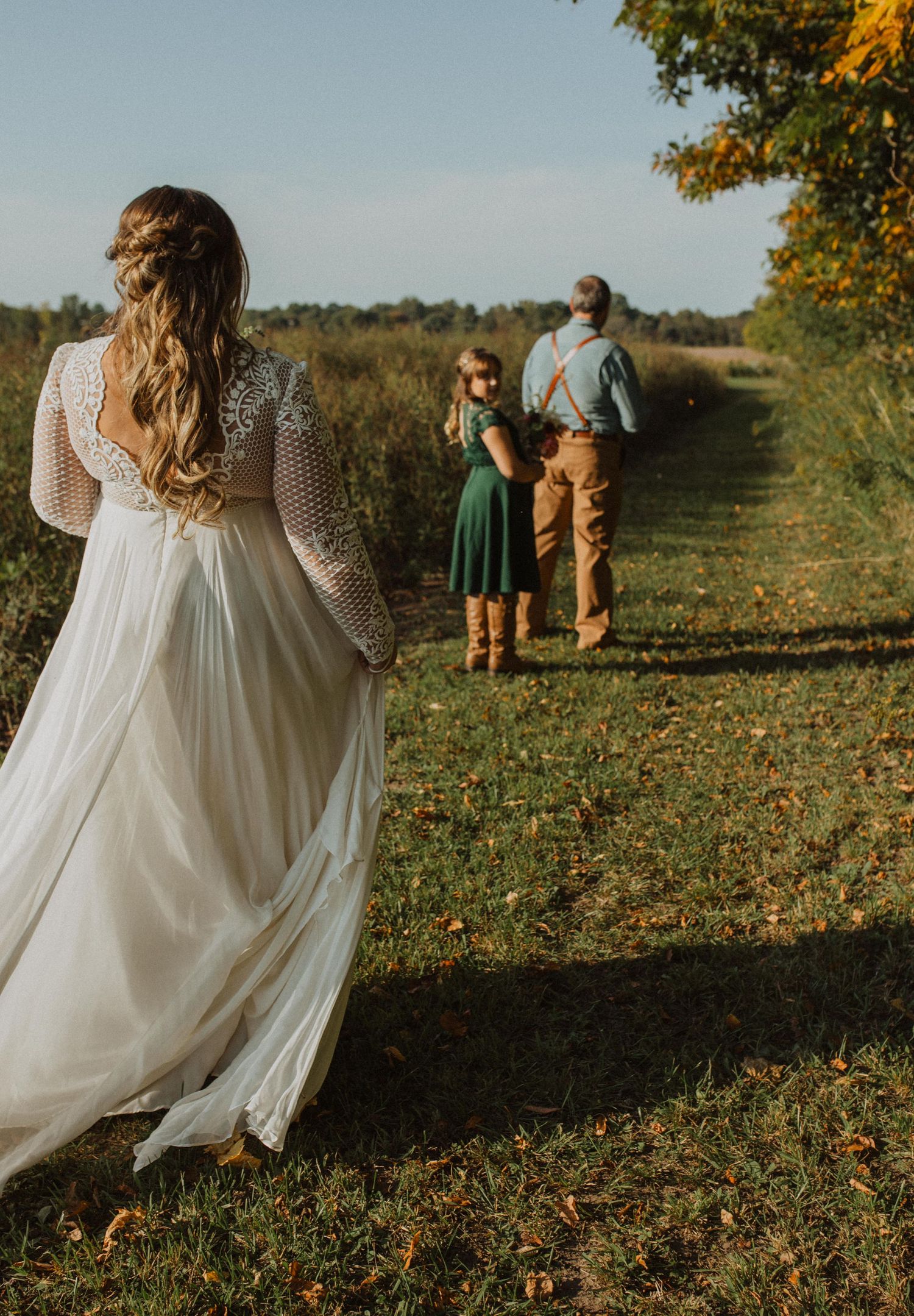 Wedding party strolling through a sunlit field during golden hour.