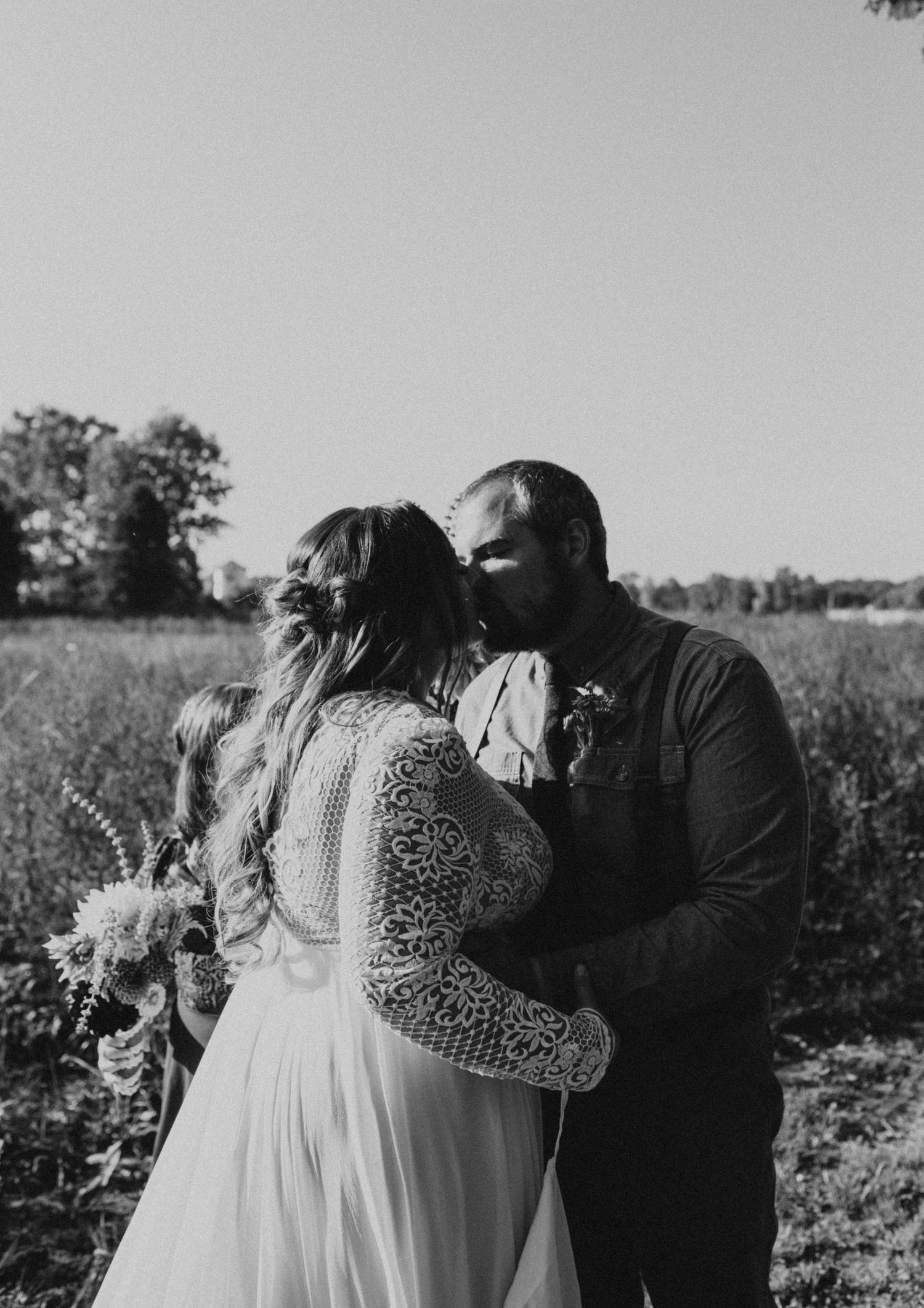 A romantic couple embraces in a field during golden hour while wearing wedding attire.