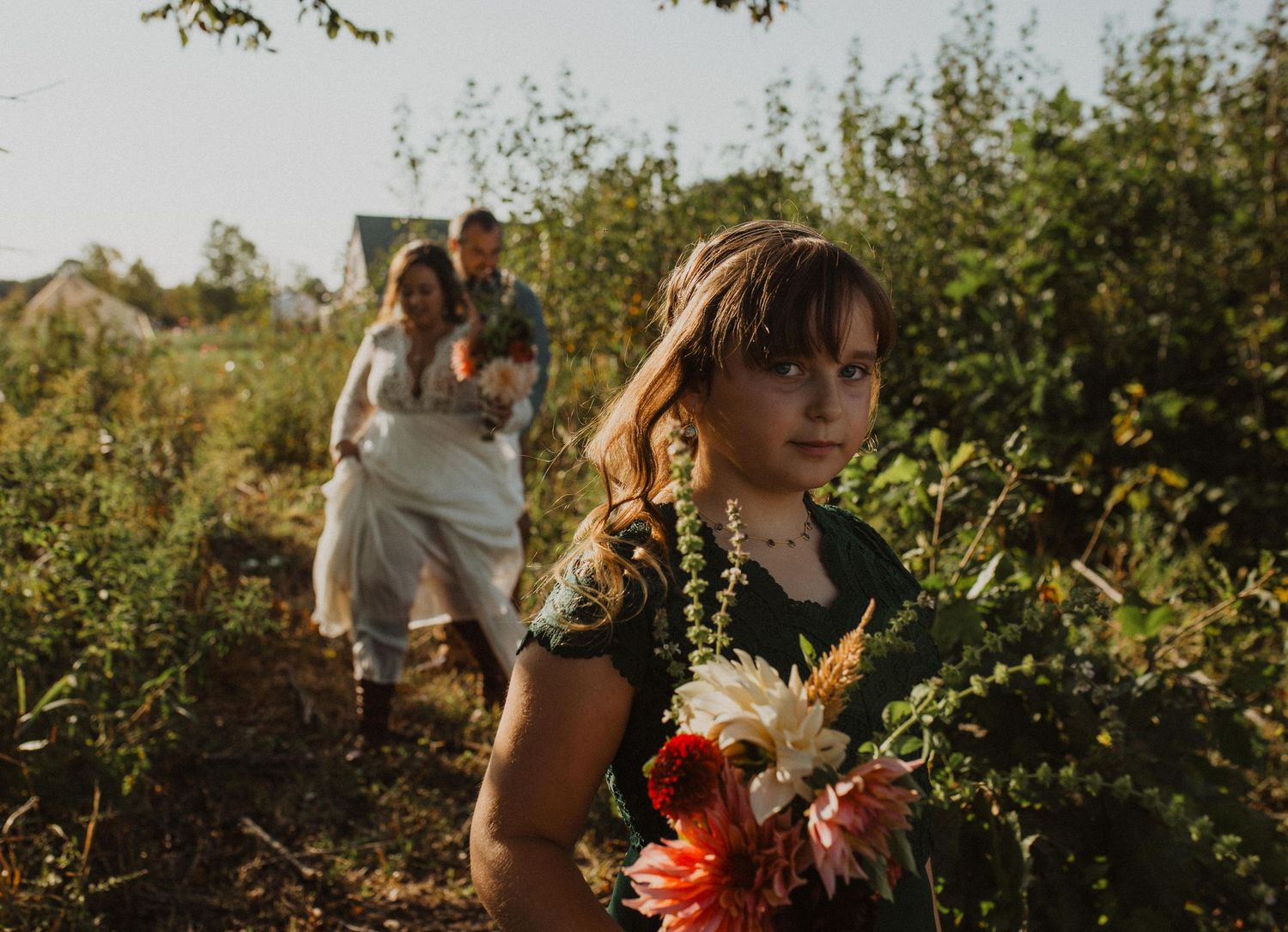 Wedding party poses in a sunlit field with autumn foliage in the background.